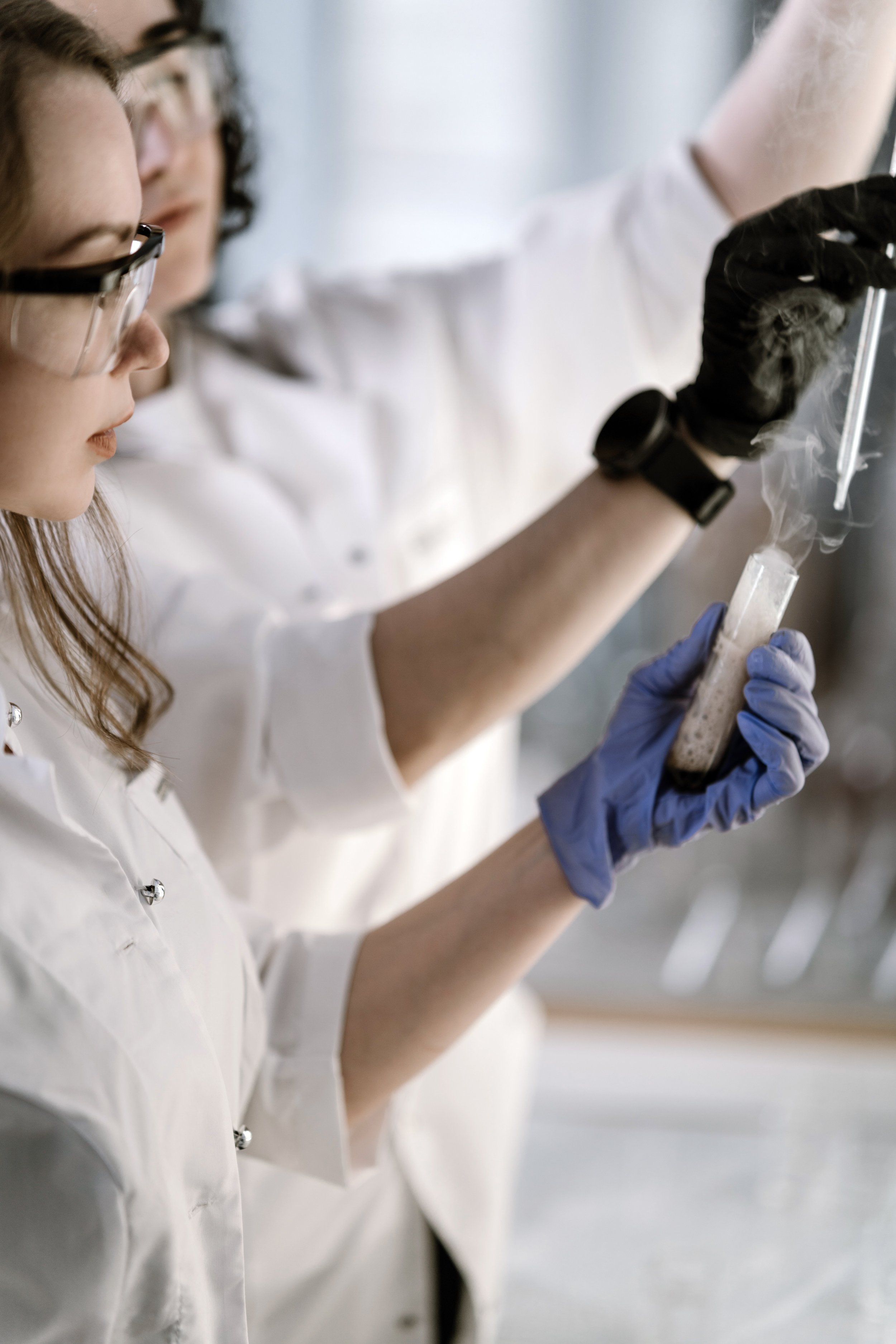 Scientists in lab coats working with test tubes containing smoke or vapor.