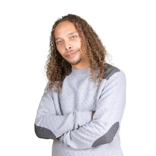 A man with long curly hair and a light beard crossing his arms, wearing a light gray sweatshirt with dark gray patches on the shoulders and elbows, smiling slightly at the camera against a plain white background.