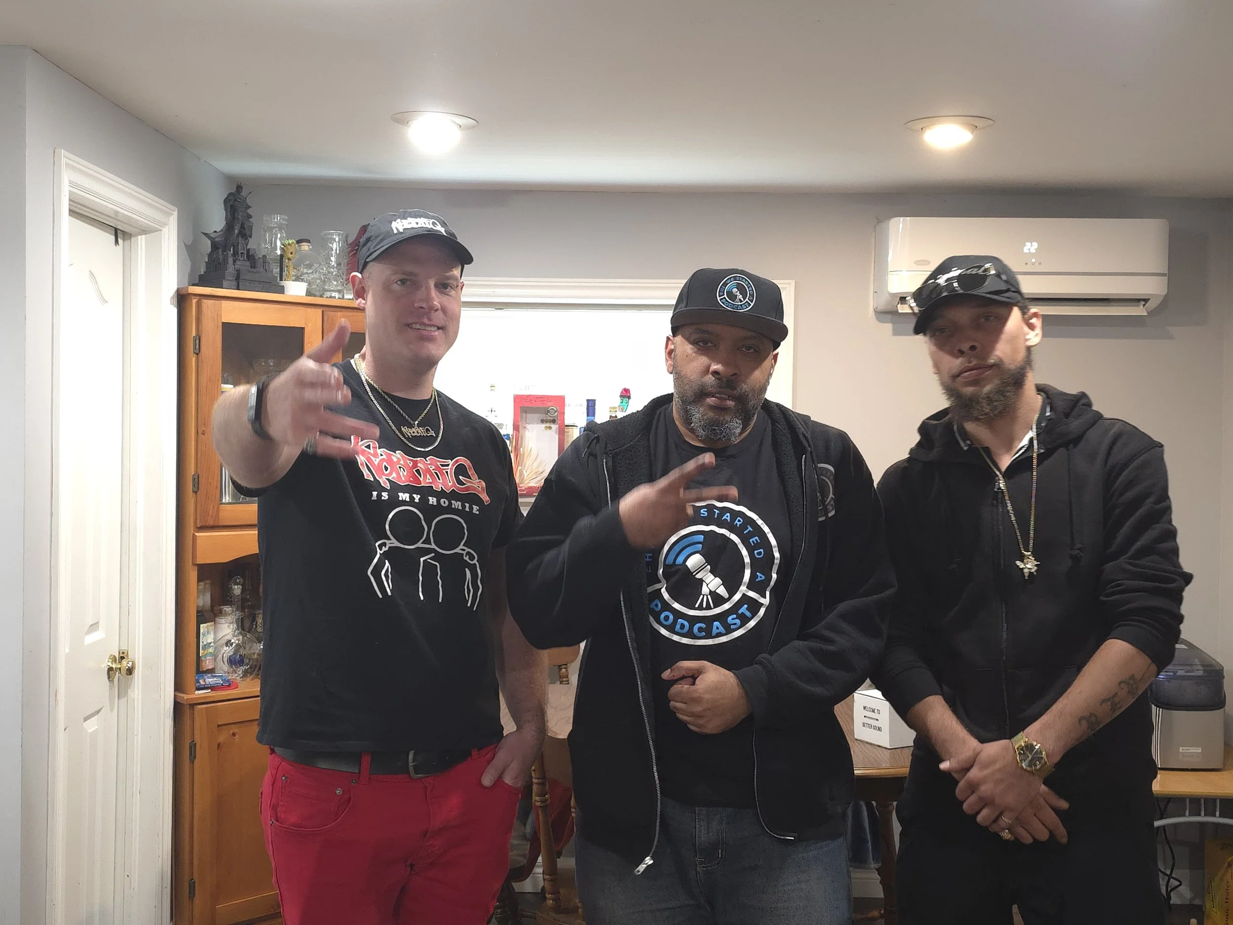 Robbie G, Jon Kizzy and Ray Rey posing together indoors, with one pointing towards the camera, wearing hats and dark clothing.