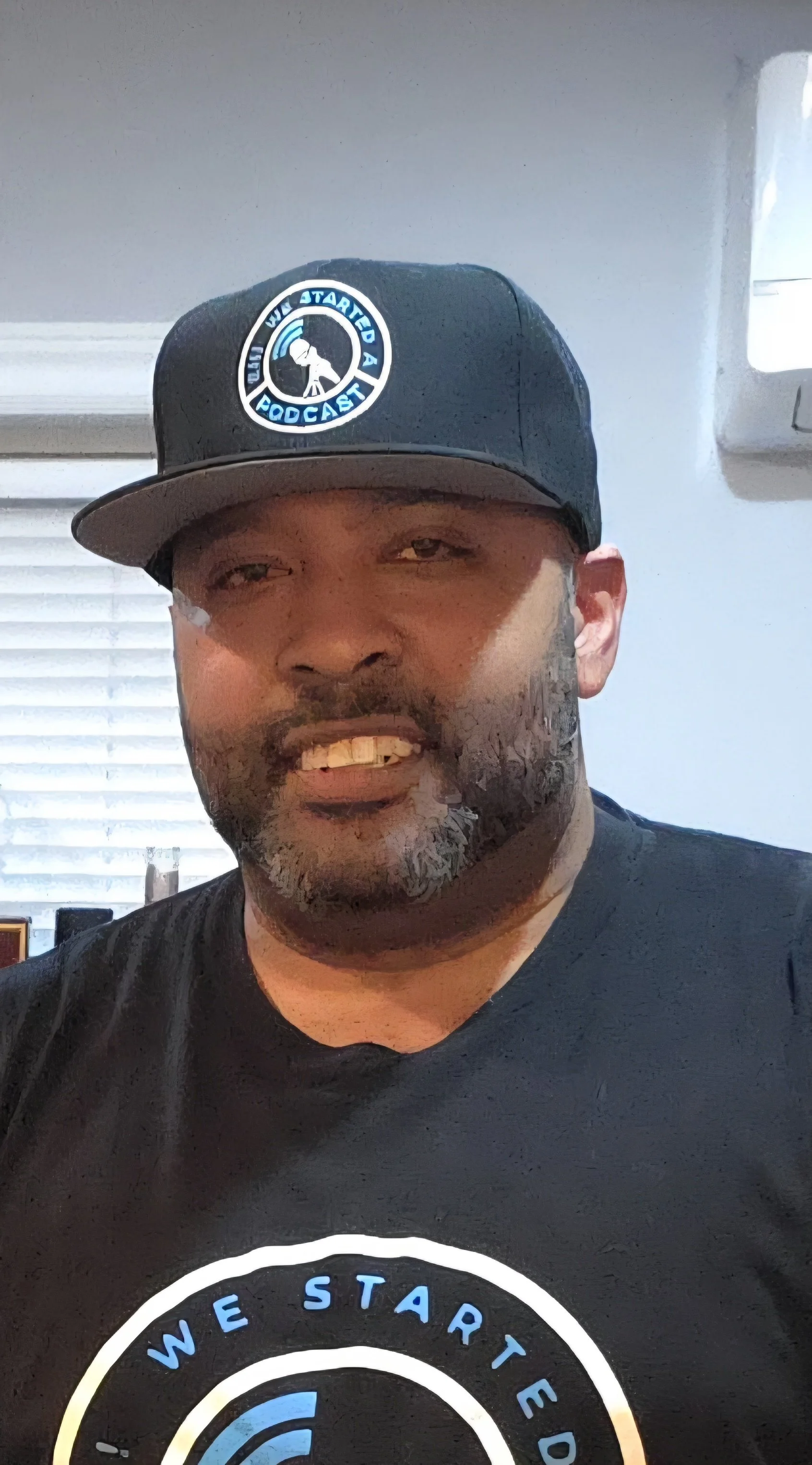 Jon Kizzy wearing a black baseball cap with the "Eh! We Started A Podcast Logo" logo and a black t-shirt with the "EH! WE STARTED A PODCAST" logo.