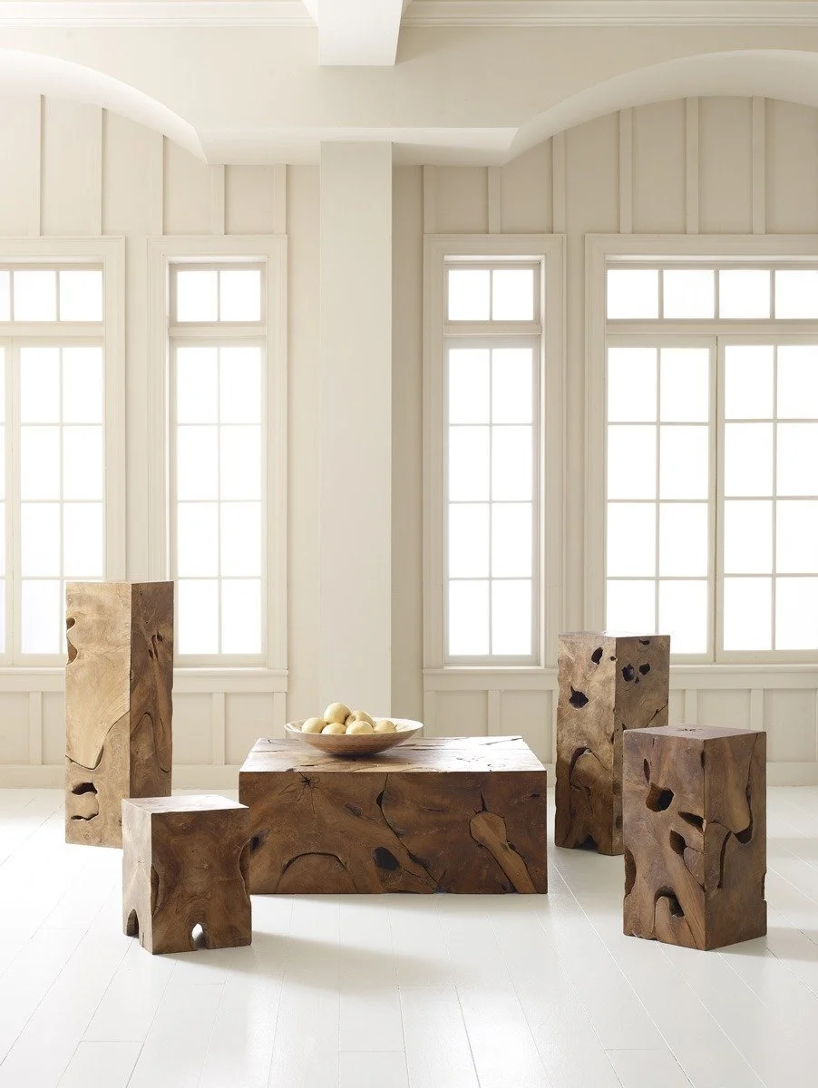 Interior room with white walls and large windows, featuring a wooden table with a bowl of apples, and four irregularly shaped wooden stools.