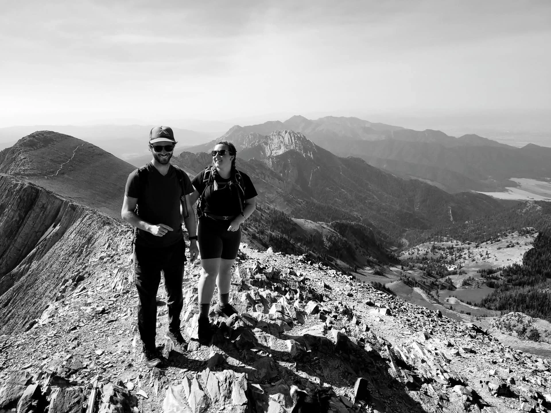 Two hikers, a man and a woman, walking on a rocky mountain trail with mountains in the background