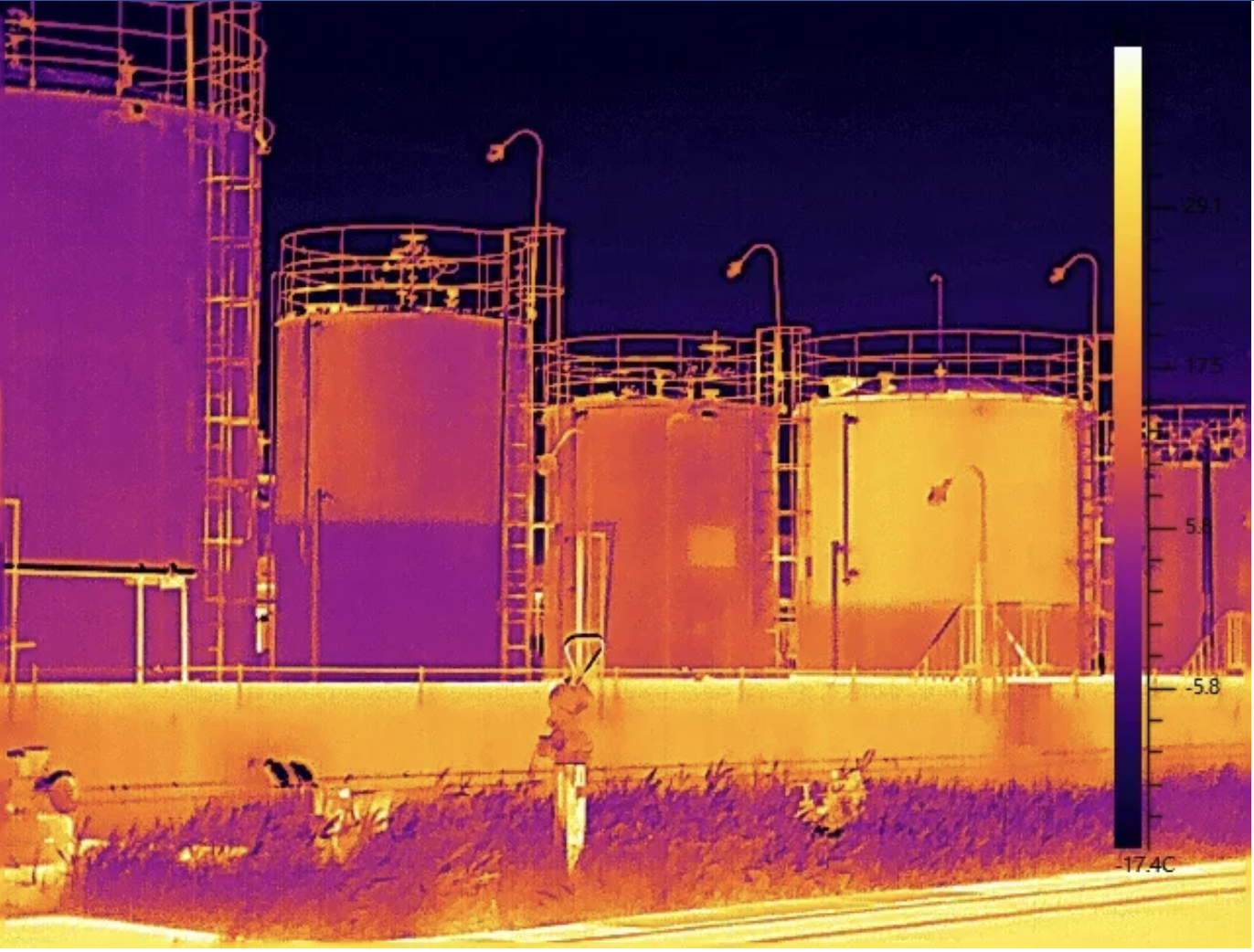 Infrared image of large industrial storage tanks with temperature scale on right side.
