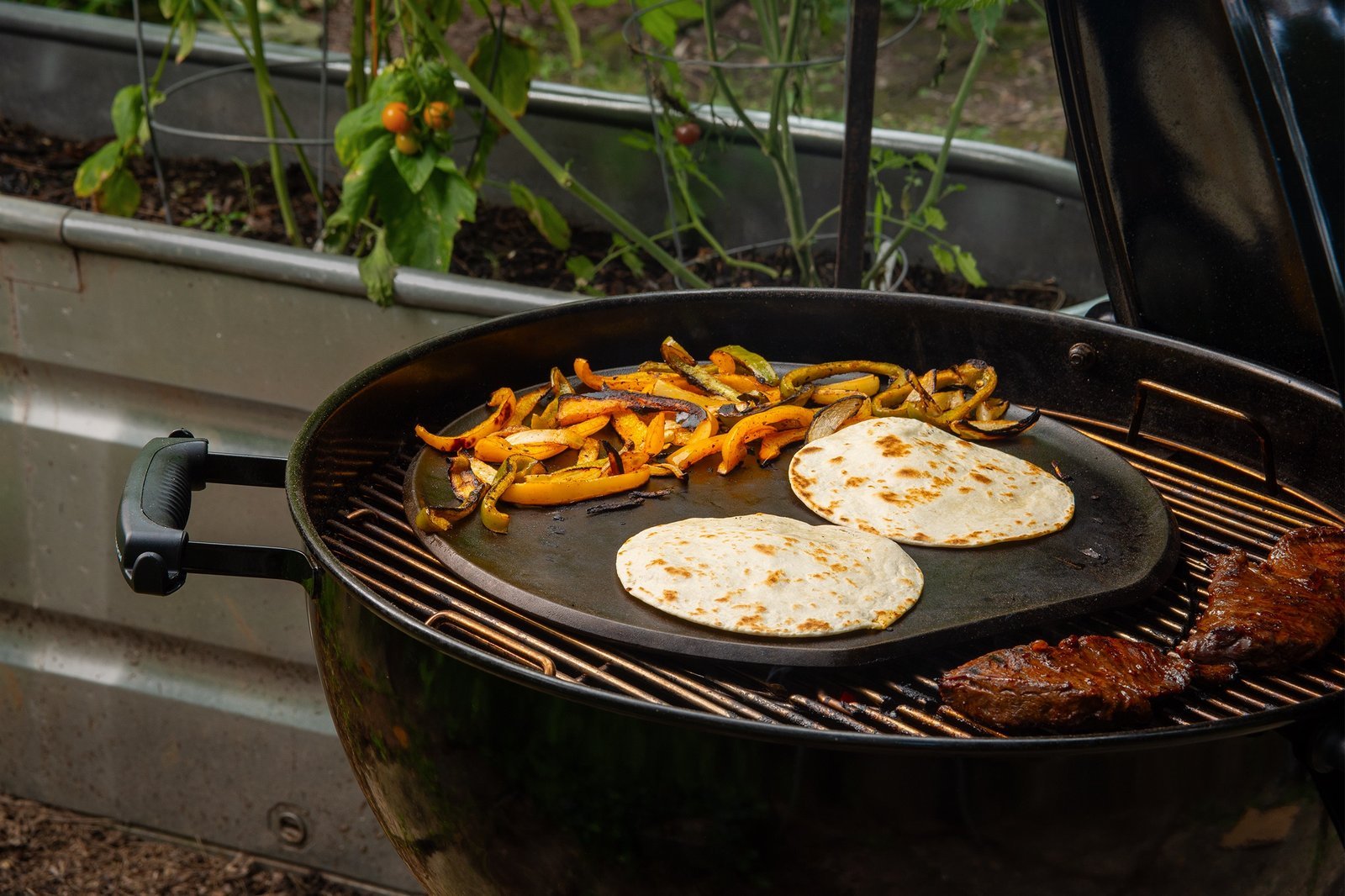 Borough Furnace cast iron pizza griddle on outdoor kettle grill with tortillas and roasted peppers