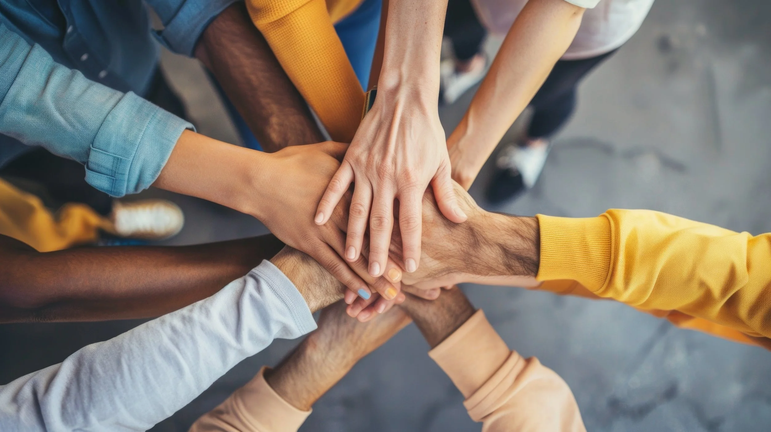 Wild Goose Studios - who we serve - Multiple hands from diverse individuals stacking together in a show of unity.