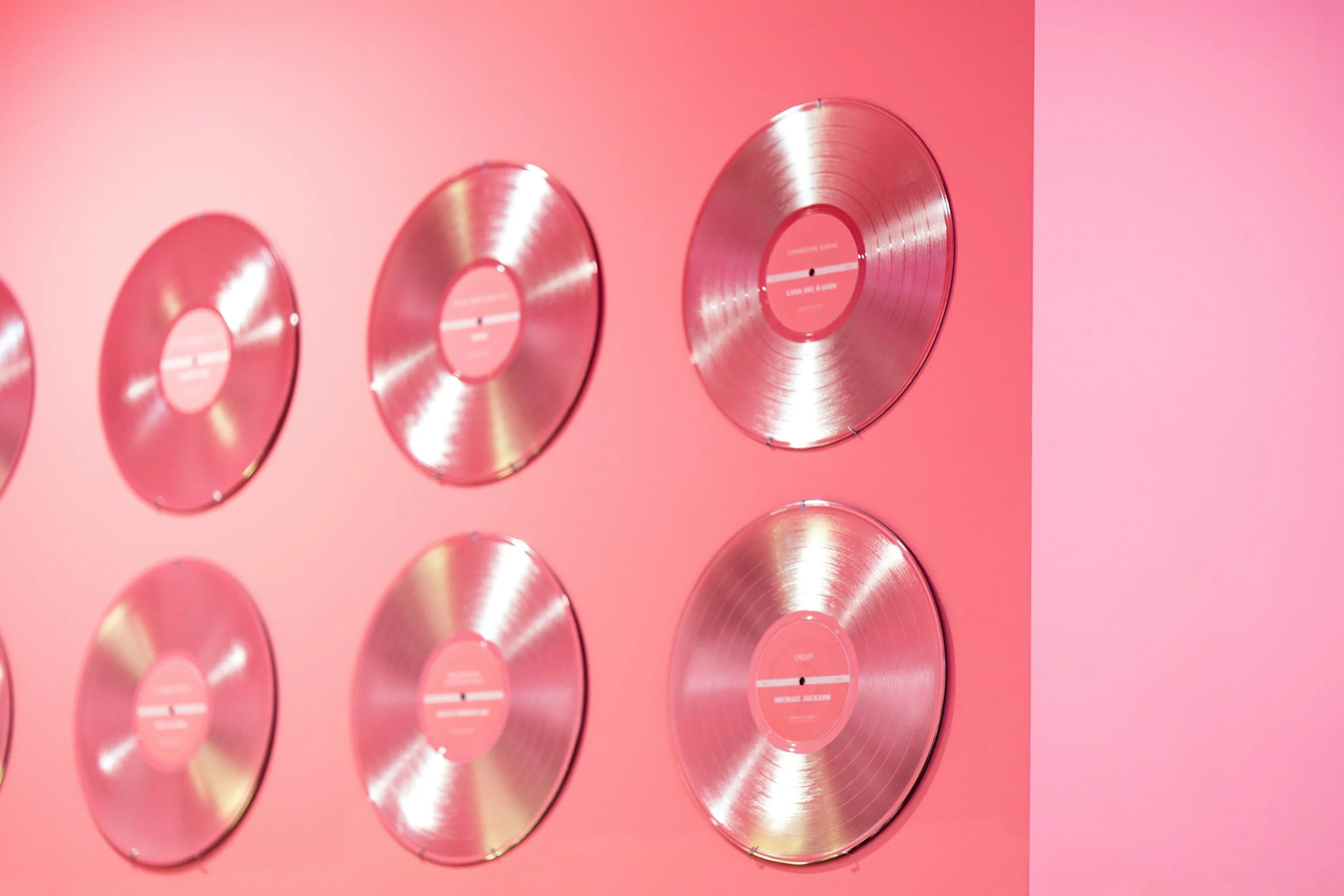 Pink wall with multiple shiny gold vinyl records displayed in a row.