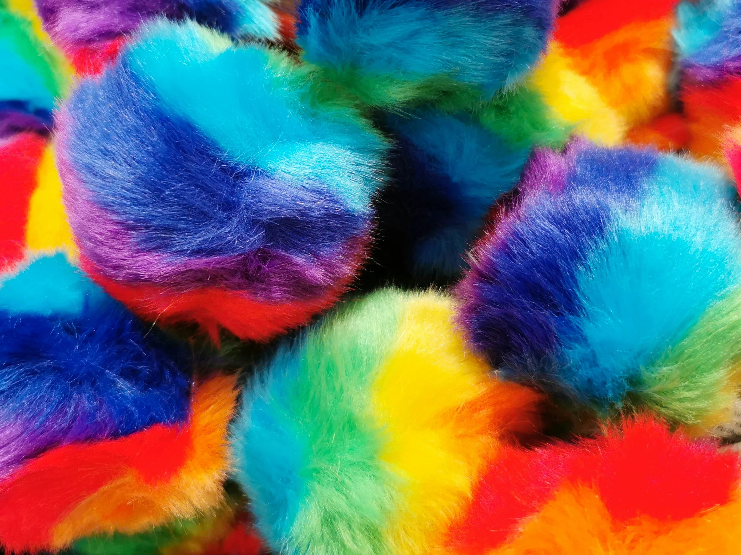 Close-up of colorful fluffy tie-dye fabric with vibrant rainbow colors including blue, green, yellow, orange, red, and purple.