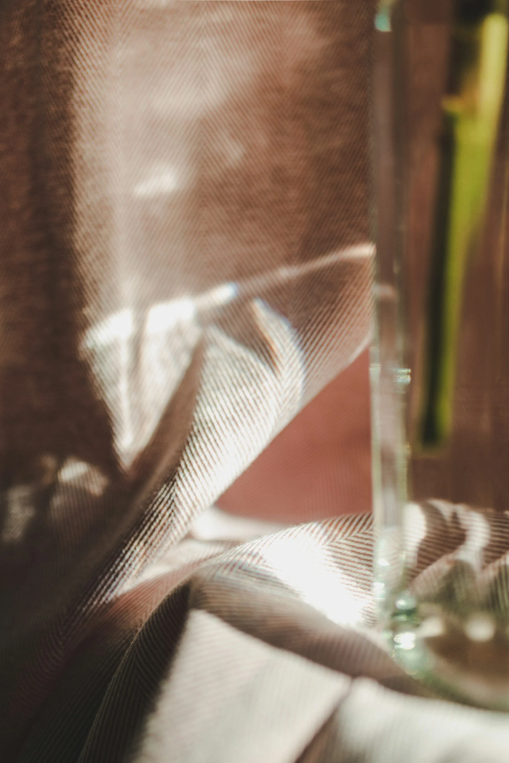 Close-up of a glass with a drink, partially covered by a patterned cloth, with sunlight creating reflections on the glass.