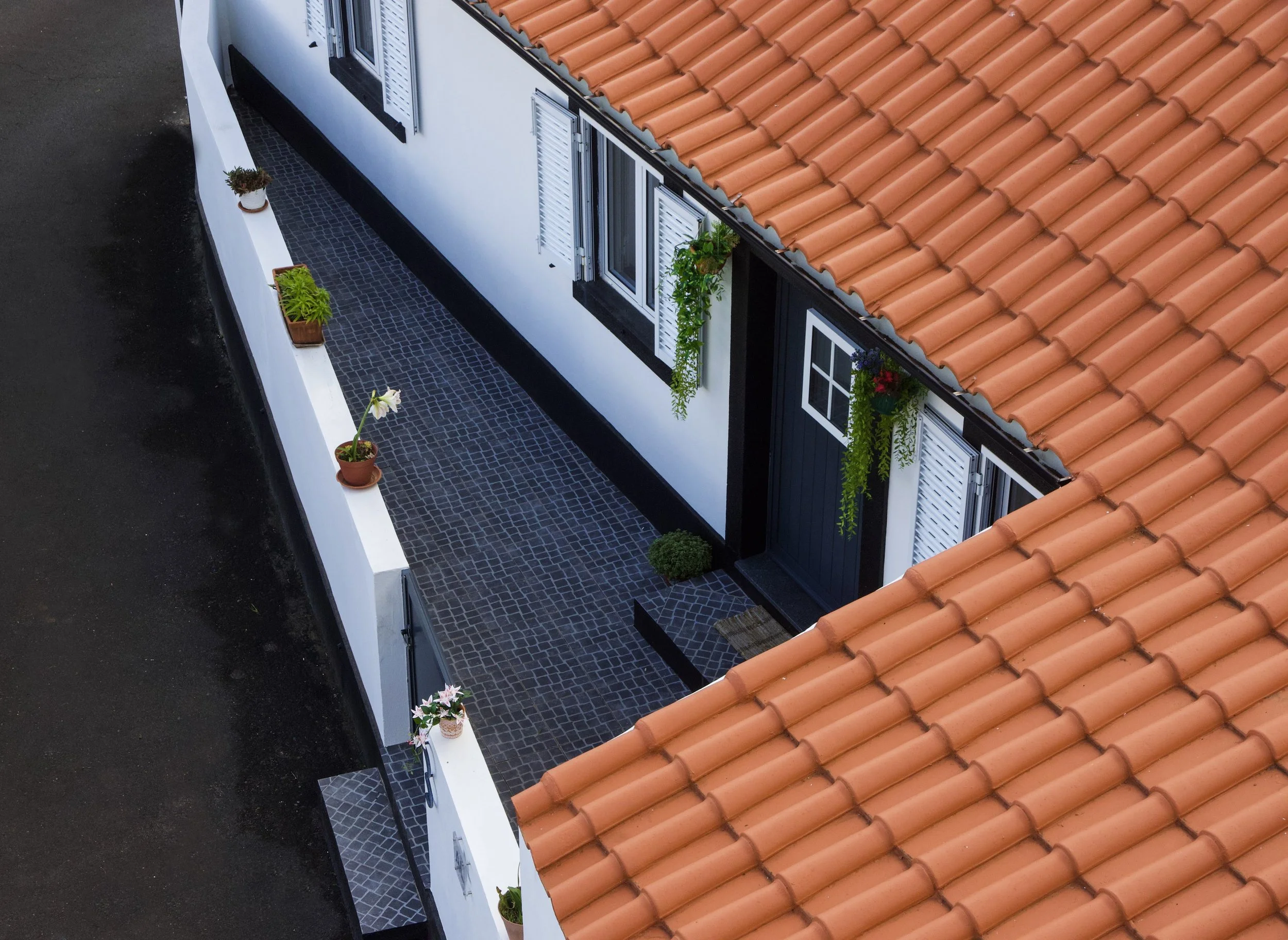 A top-down view of a building's balcony with potted plants and a reddish-tiled roof.