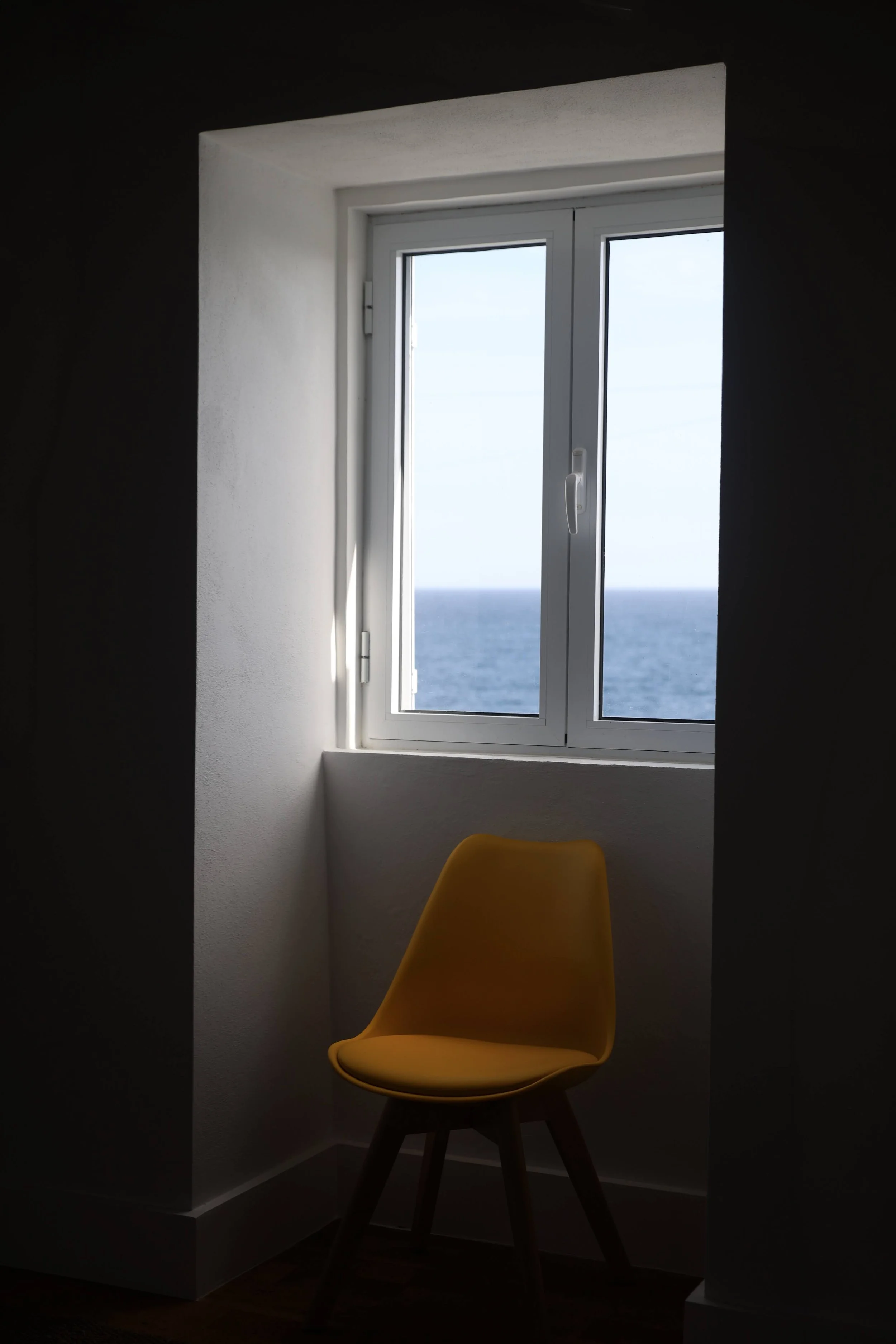 A yellow chair in a dimly lit room with a window showing an ocean view outside.