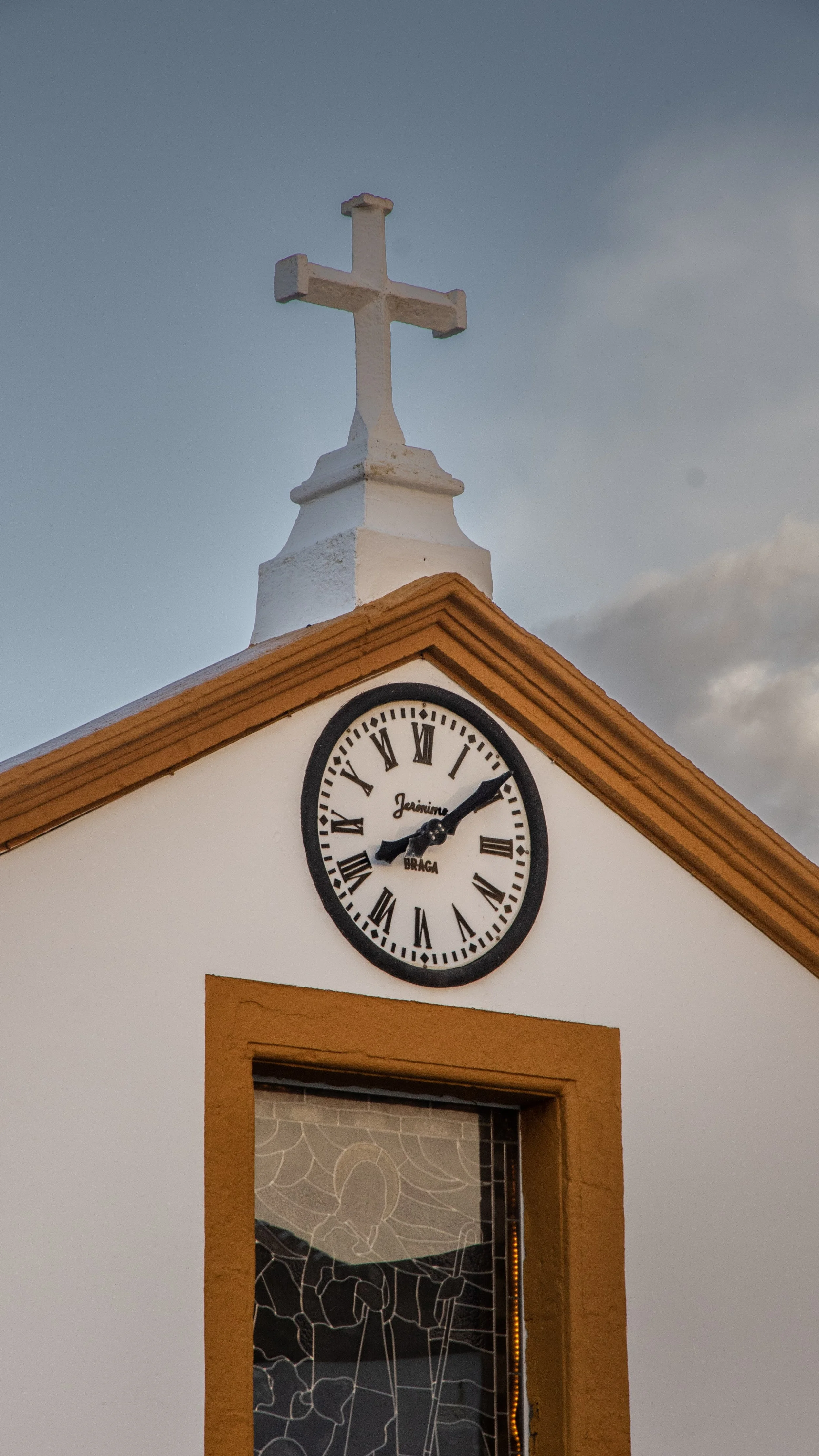 A church steeple with a cross on top, a clock showing 9:09, and a stained glass window below, framed with a mustard yellow border.