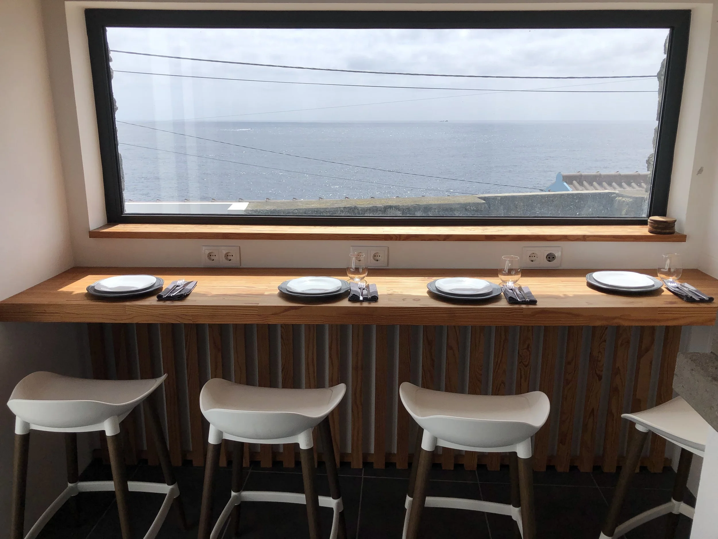 Table with four white chairs in front of a large window overlooking the ocean on Terceira Island, Azores on a cloudy day.