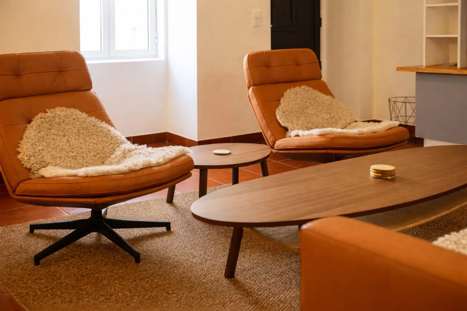 Living room with two orange leather lounge chairs with fluffy beige pillows, a small round wooden side table, a large wooden coffee table, and a brown textured area rug.