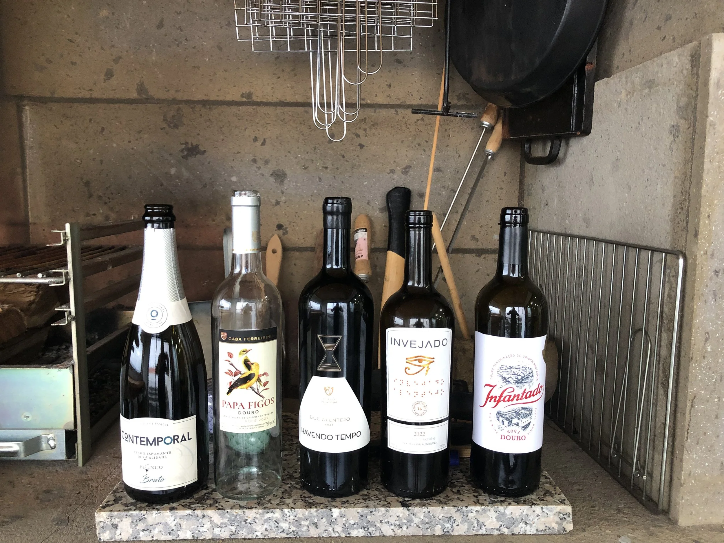 Five bottles of wine placed on a granite countertop, with a wine rack and a black grill in the background.