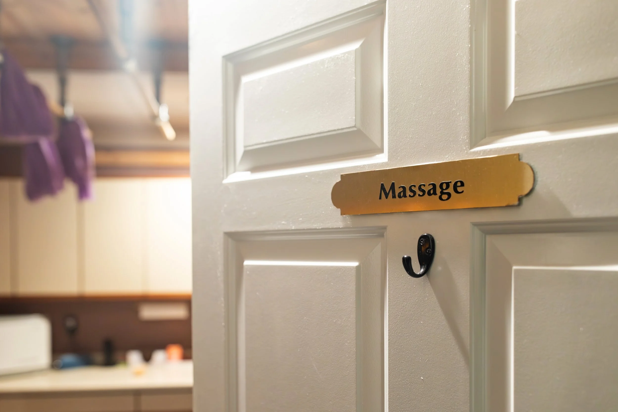 Close-up of a white door with a small gold sign labeled 'Massage' attached underneath a door handle hook.
