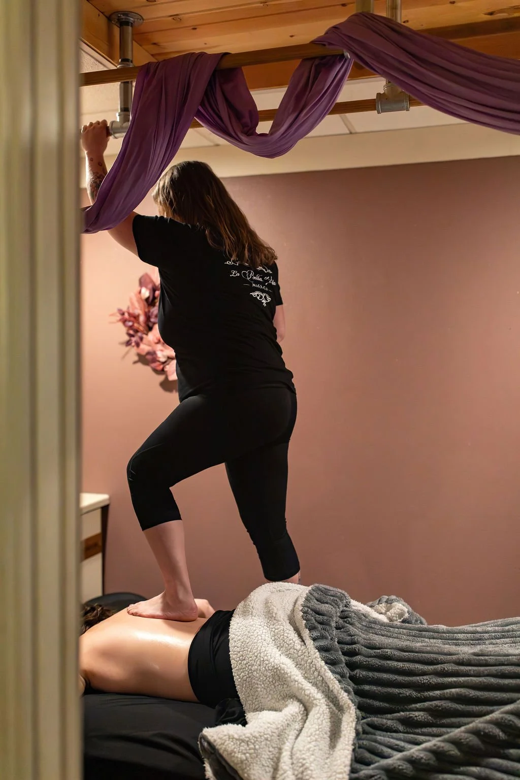 A person receiving a massage from a massage therapist in a spa room with pink walls and purple drapes hanging from the ceiling.