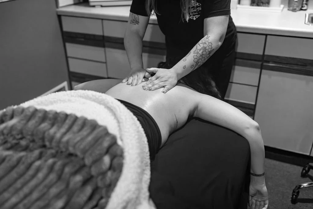A person giving a massage to another person lying face down on a massage table in a clinical setting.