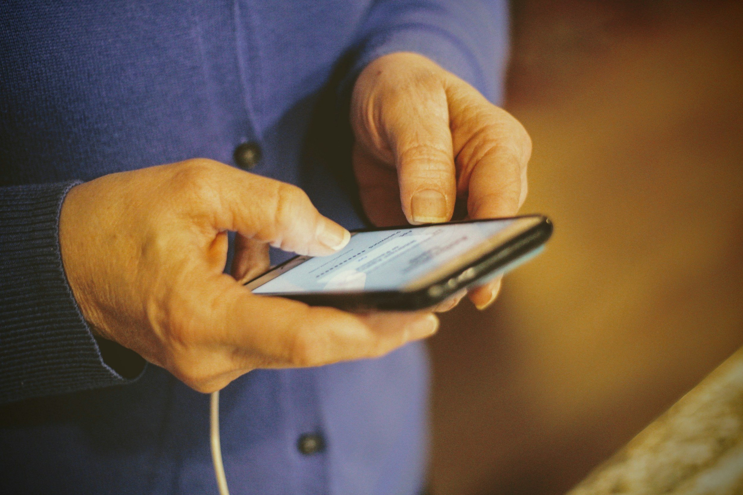Close-up of an elderly person's hands using a smartphone, wearing a dark blue sweater.