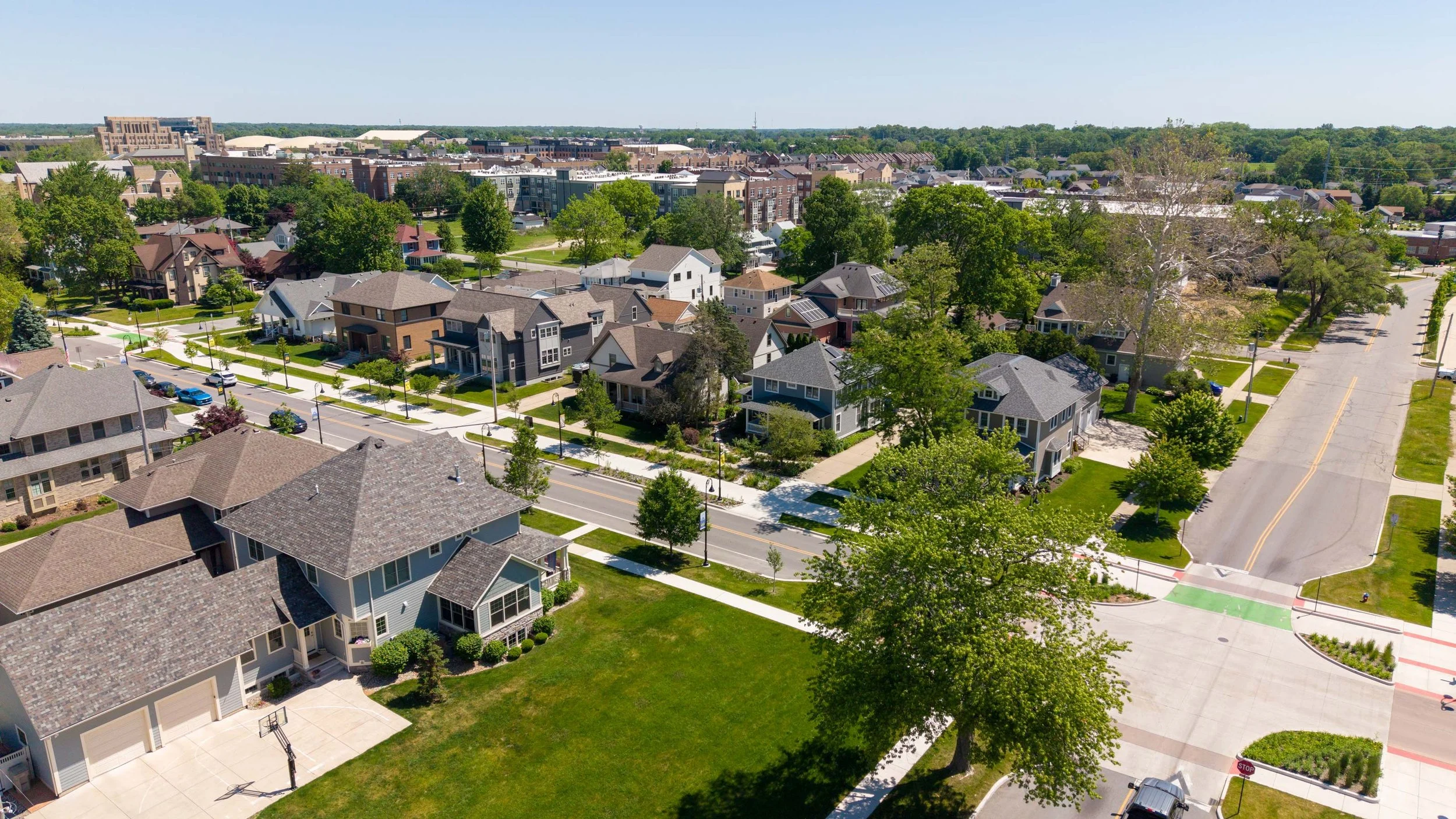 Aerial view of a suburban neighborhood with houses, trees, and streets on a sunny day.