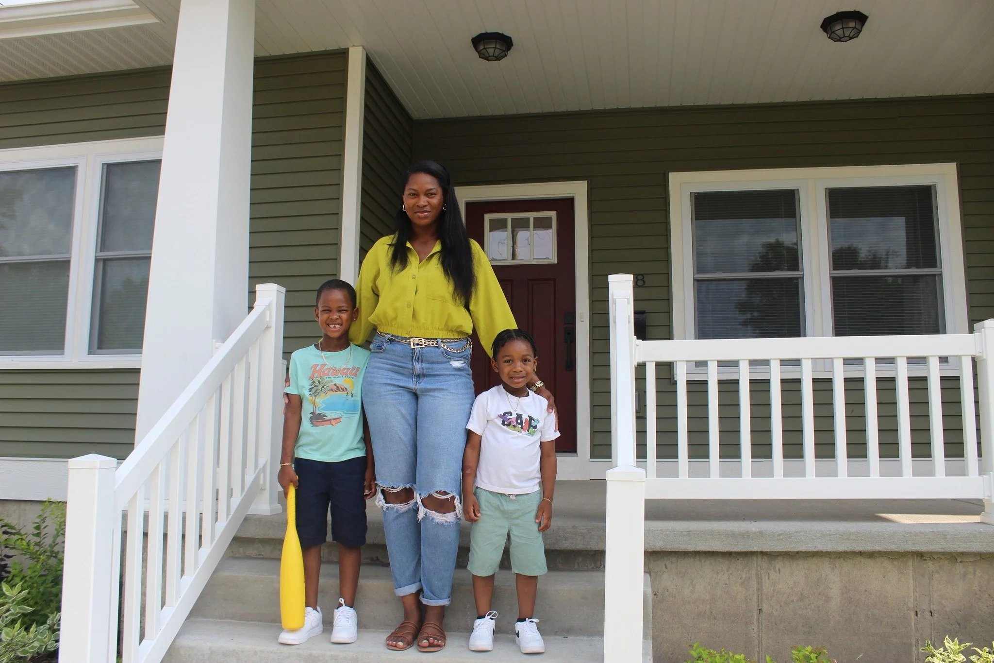 A woman and three children standing on the front porch of a house, smiling at the camera.