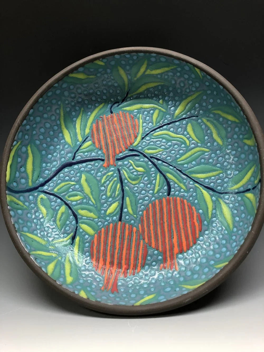 Decorative ceramic plate with a painted design of red cherries and green leaves on a blue textured background.