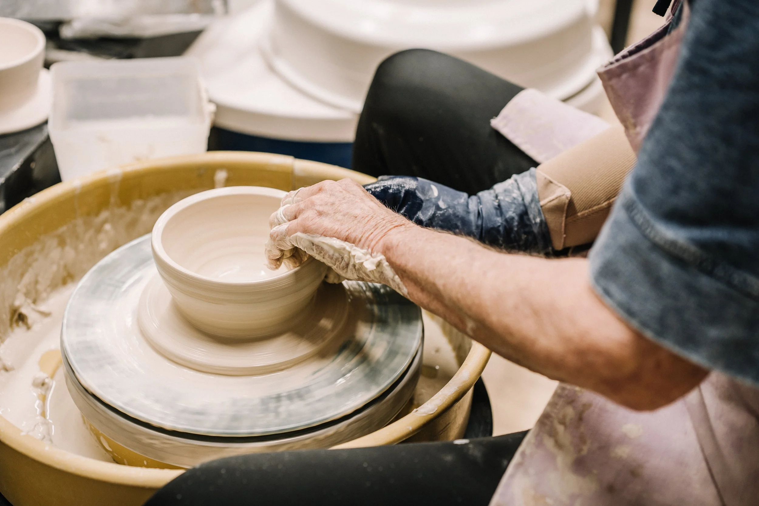 A person shaping a ceramic bowl on a pottery wheel, hands covered in clay in a pottery studio.