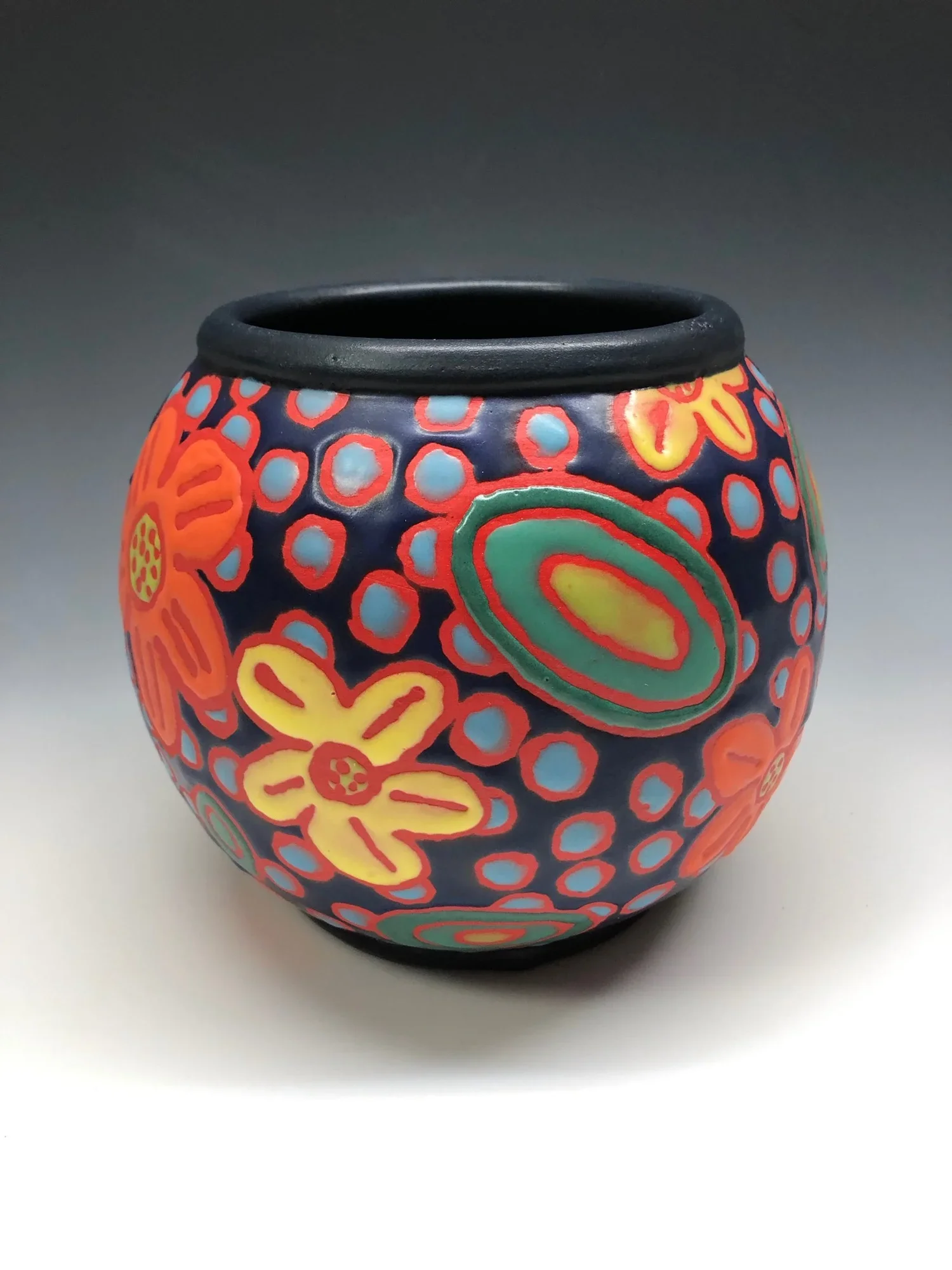 A colorful, round ceramic vase decorated with floral and abstract patterns in red, yellow, green, and blue colors.