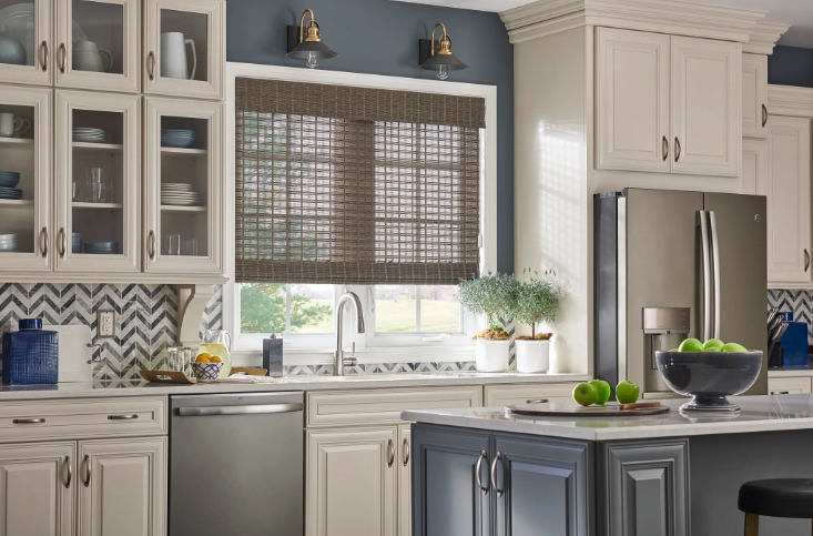 Woven wood shade on a kitchen window above the sink in a transitional kitchen with cream cabinets and a patterned tile backsplash