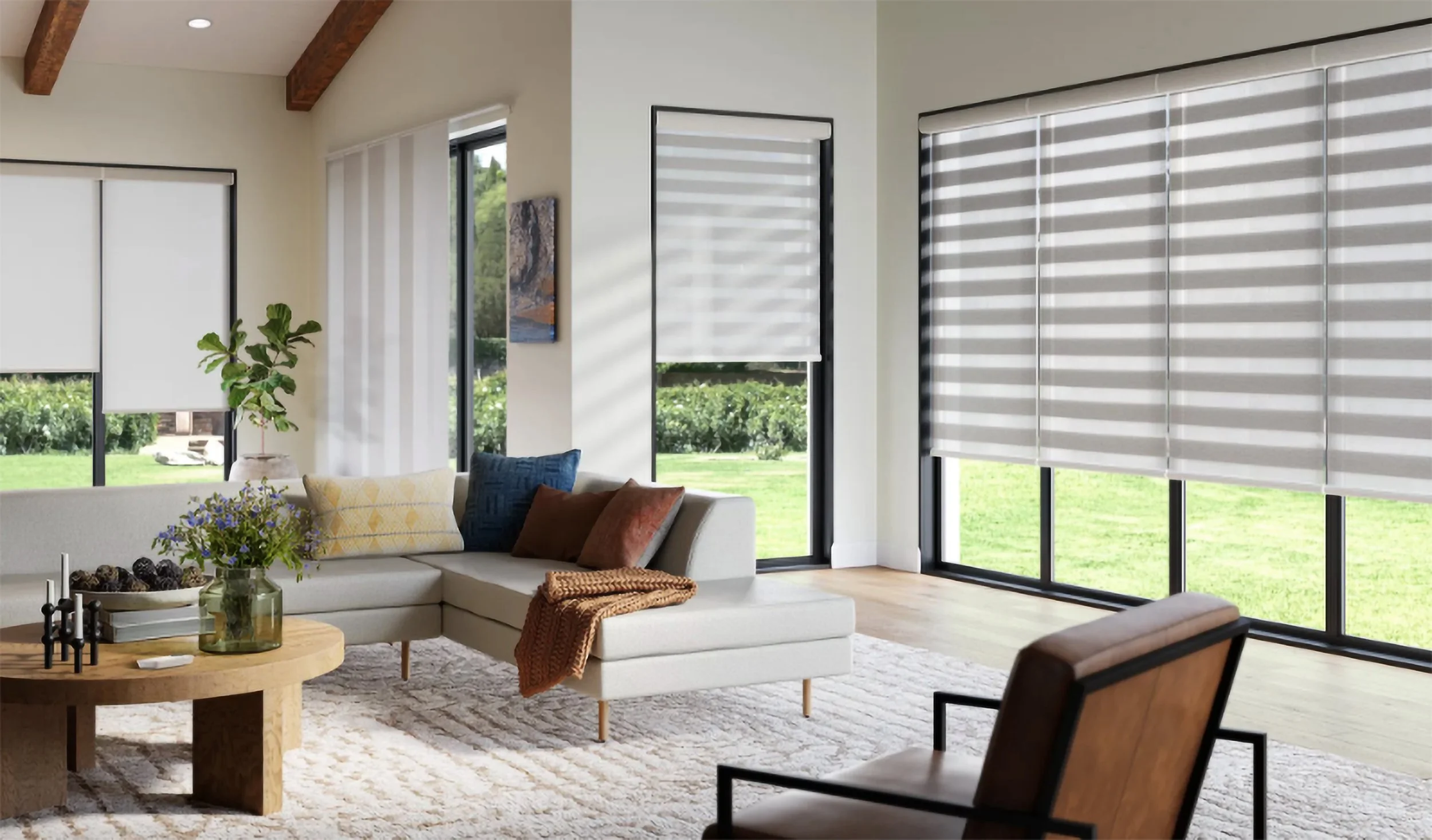 Light gray layered sheer shades on floor-to-ceiling windows in a modern open living room with wood beam ceilings and a view of green outdoor space