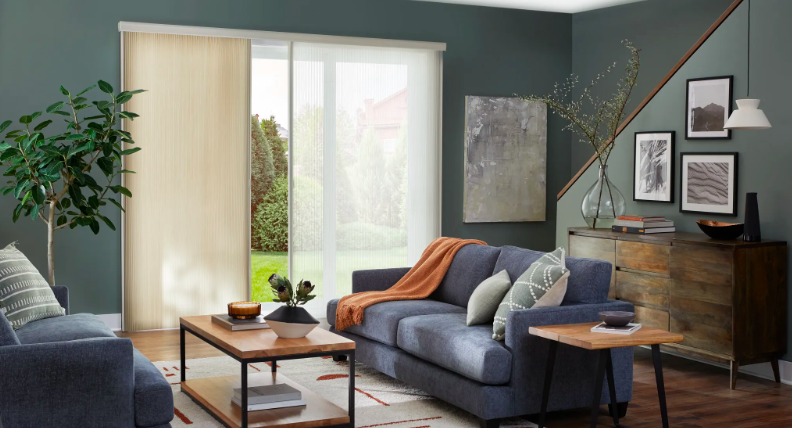 Cream panel track blinds on a sliding glass door in a modern living room with dark green walls and a blue sofa