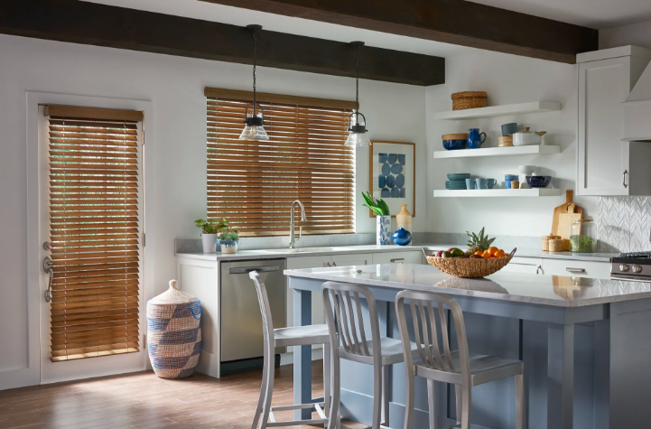 Wood blinds on kitchen windows and a glass door in a bright farmhouse-style kitchen with white cabinets and exposed ceiling beams