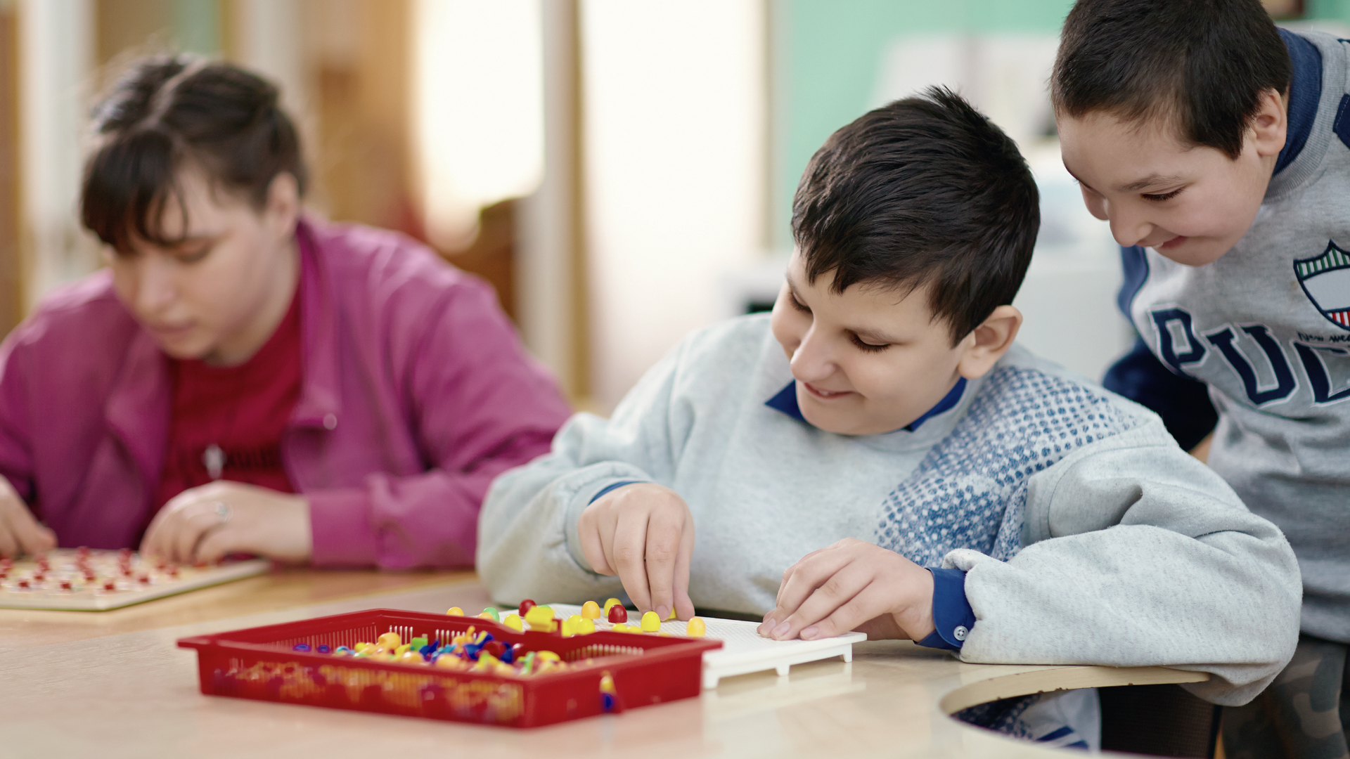 Three children and an adult playing a board game at a table in a classroom.