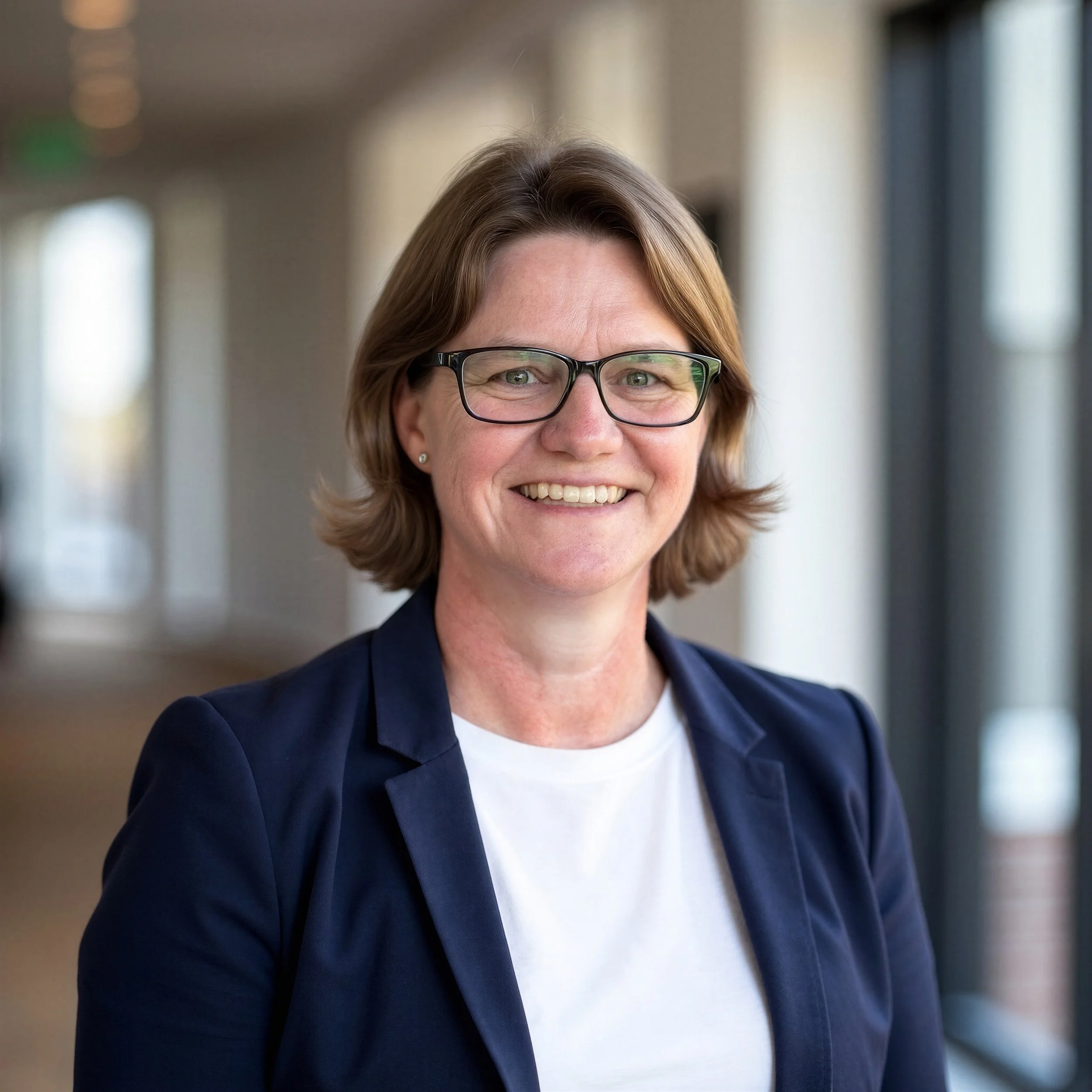 Amanda (Mandy) Robinson, Founder and Principal of Trillium Enterprise Leadership, navy blazer and standing in front of a blurred office background.