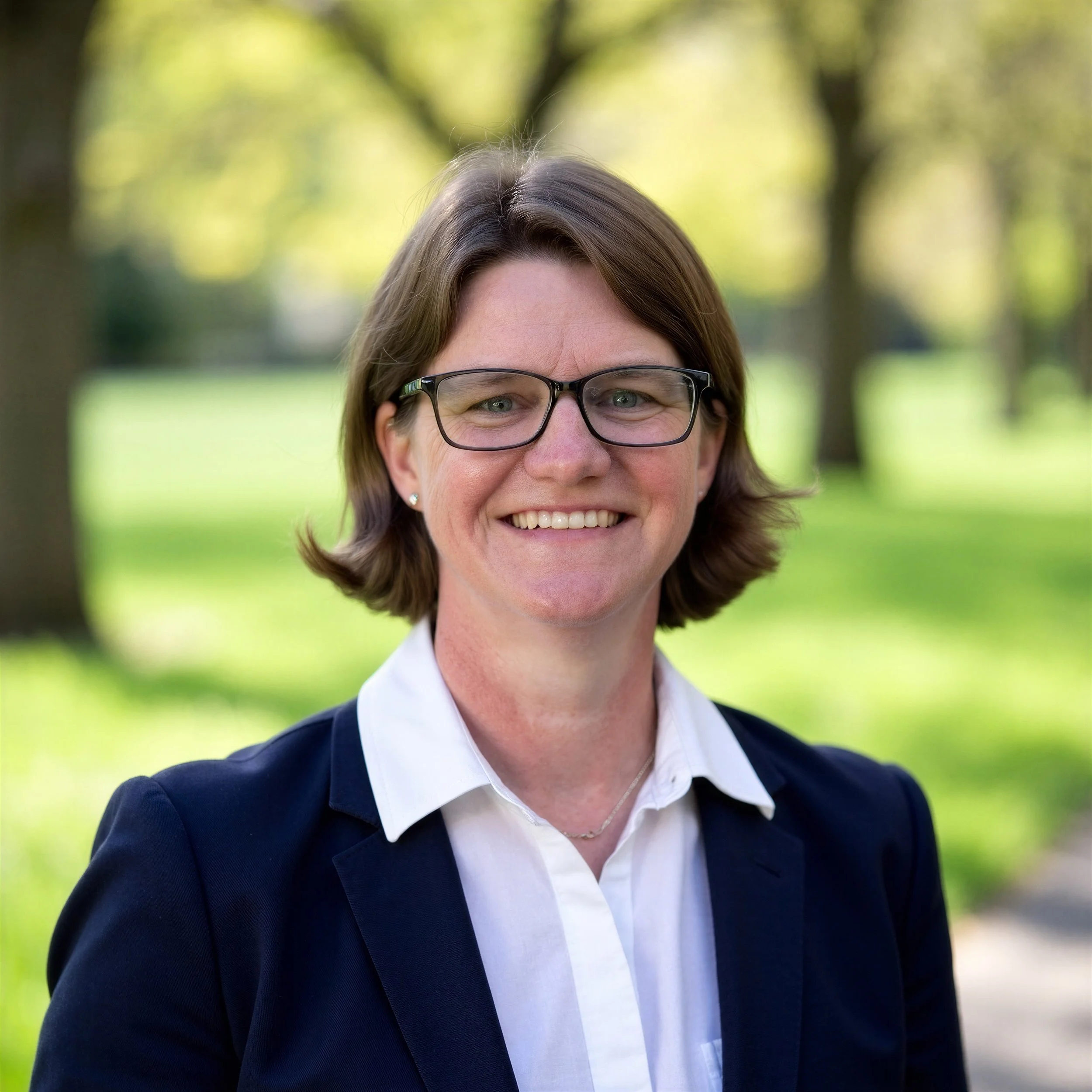 Amanda (Mandy) Robinson, Founder and Principal of Trillium Enterprise Leadership, wearing a white button-up shirt and navy blazer and standing in front of a blurred landscape background.