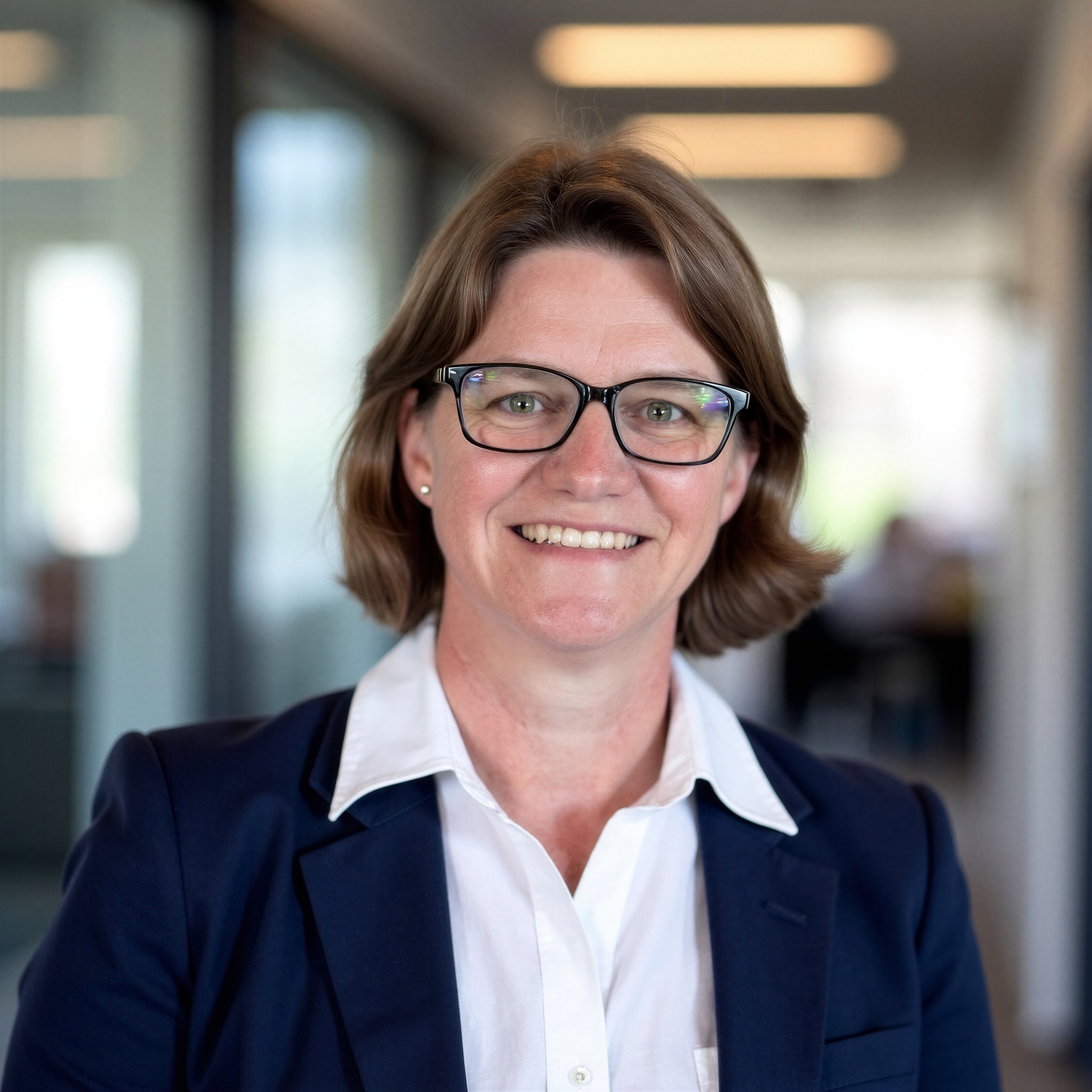 Amanda (Mandy) Robinson, Founder and Principal of Trillium Enterprise Leadership, wearing a white shirt and navy blazer and smiling in front of a blurred office space.
