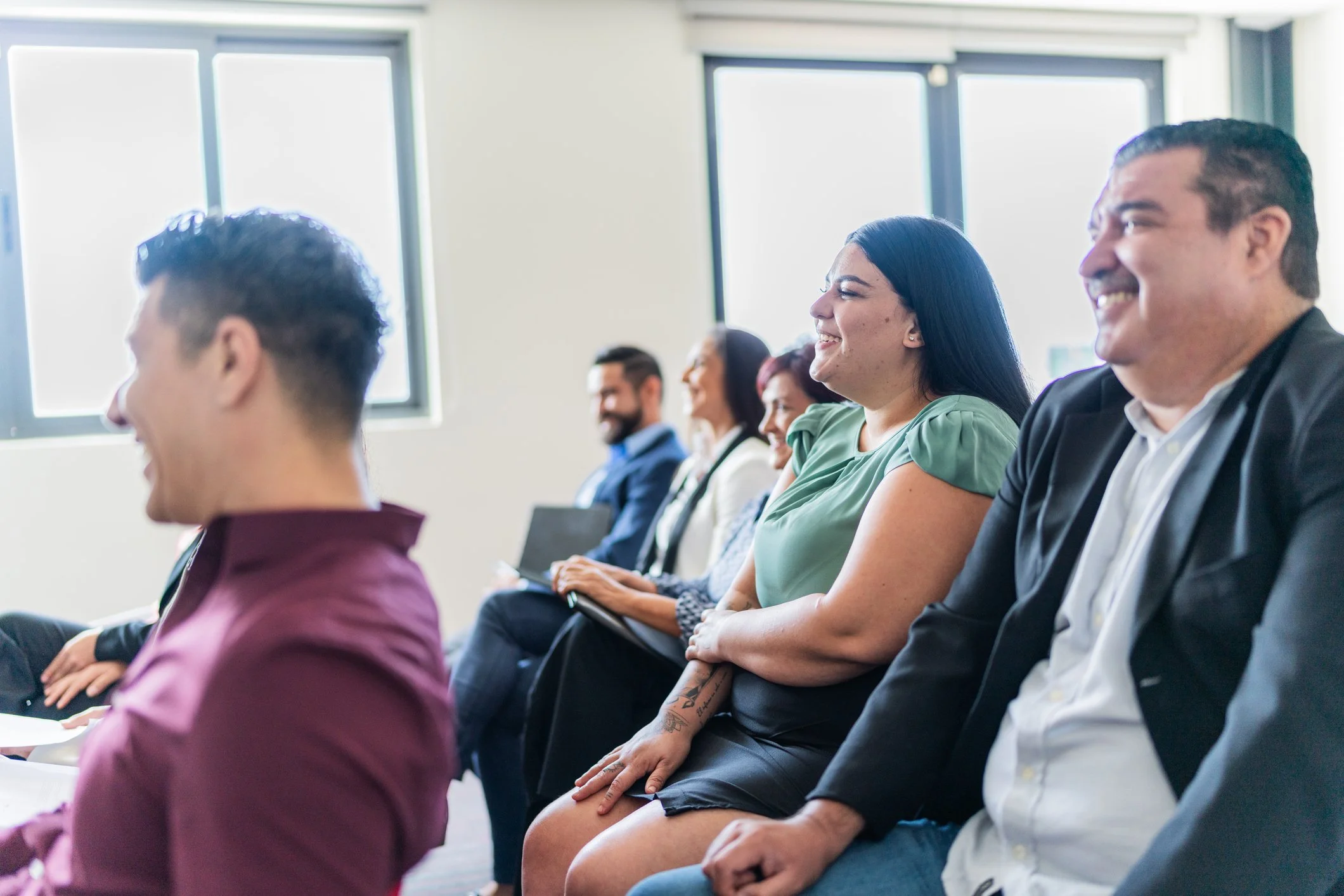 Side angle view of a smiling audience sitting in rows of chairs, listening and laughing during a corporate seminar or business conference presentation.