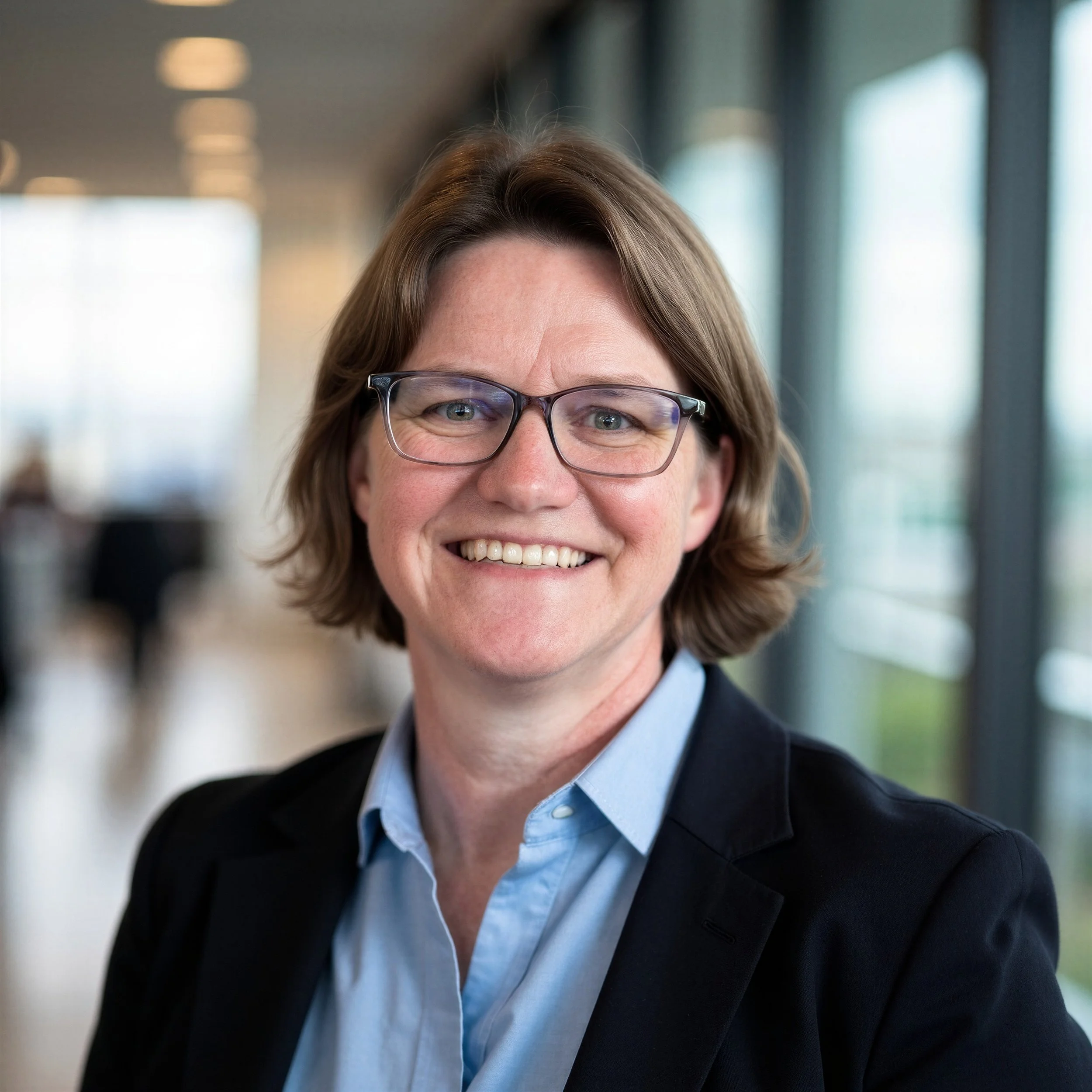 Amanda (Mandy) Robinson, Founder and Principal of Trillium Enterprise Leadership, wearing a blue button-up shirt and black blazer and standing in front of a blurred office background.