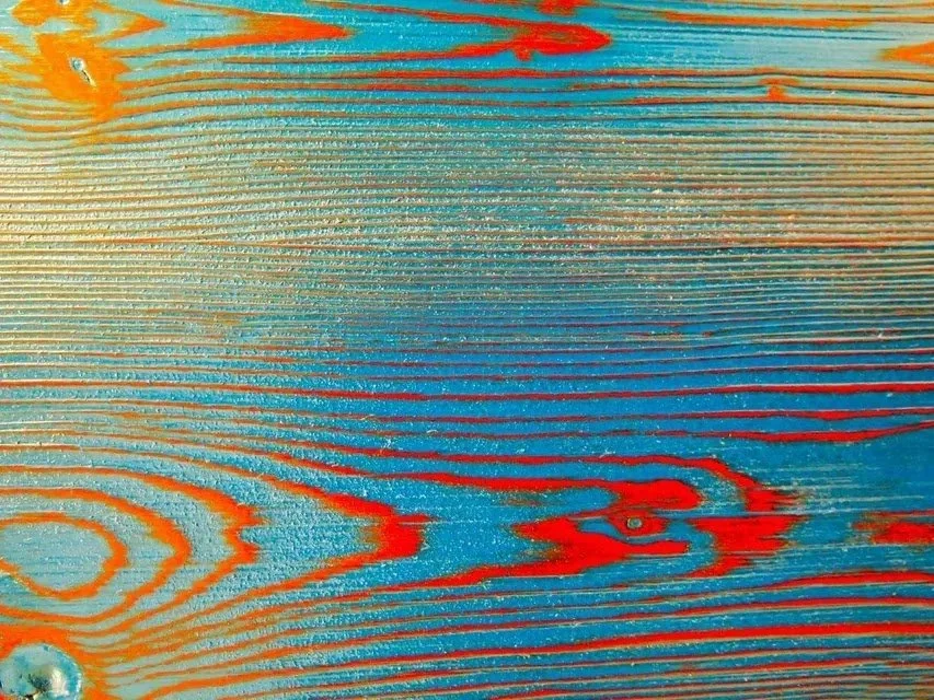 Close-up of a wooden surface stained in light blue with red and orange streaks