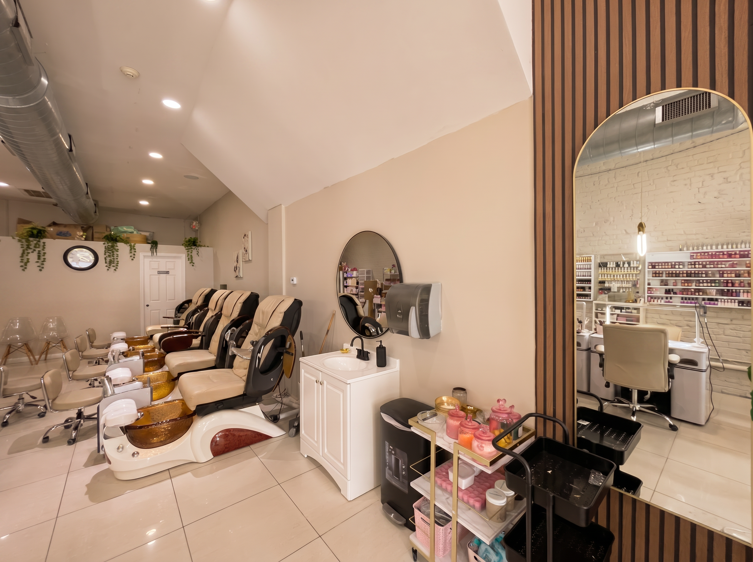 Sala de manicura y pedicura con sillas de masaje, pilas de agua, equipo de uñas y mesas con productos de belleza.