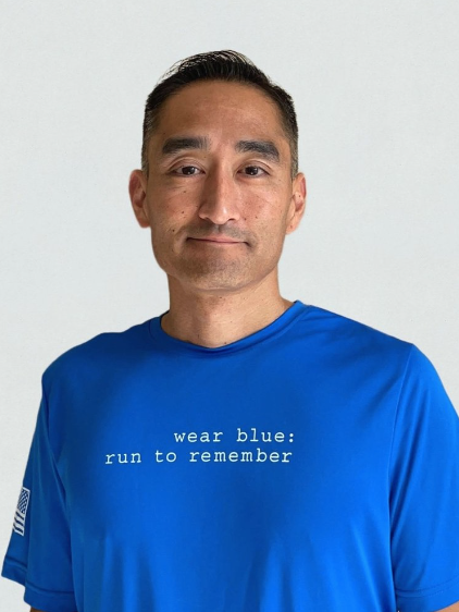 Man wearing a blue t-shirt with the text "wear blue: run to remember" printed on it, standing against a light-colored background.