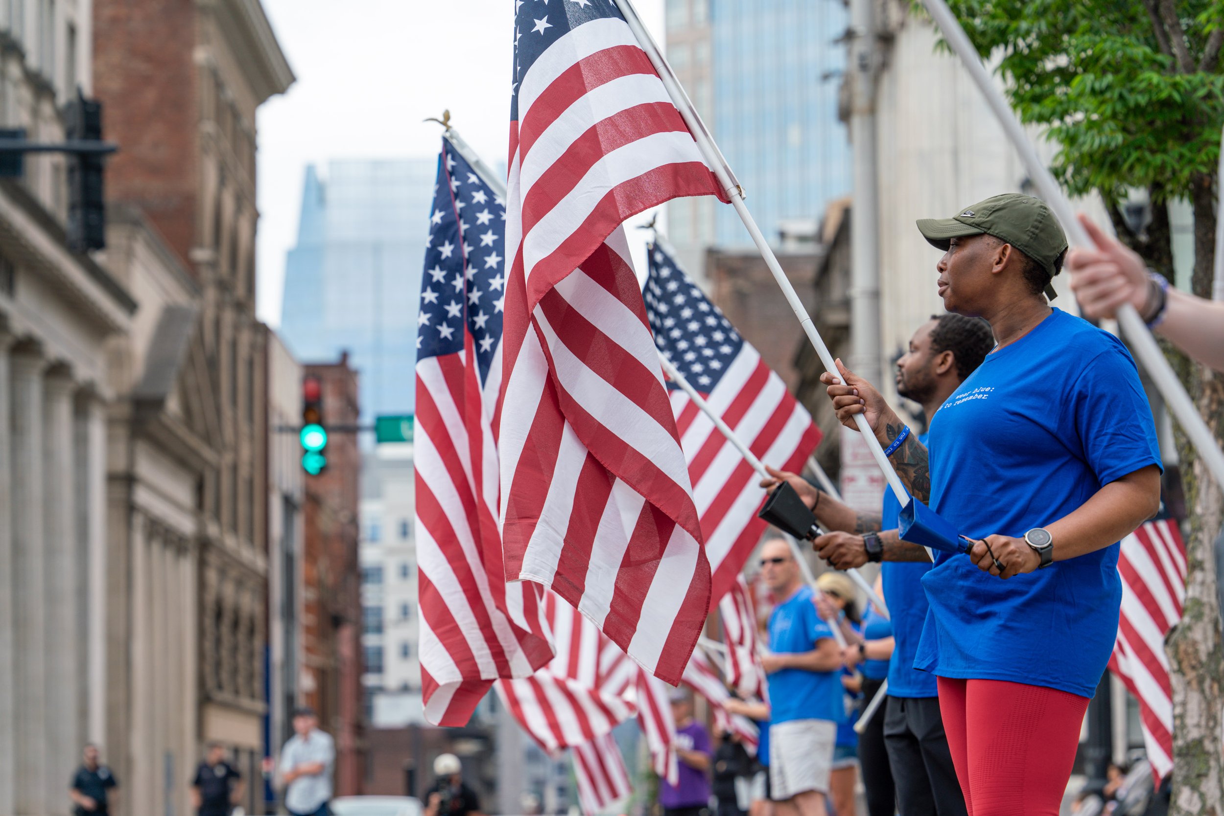People participating in a patriotic event on a city street, holding American flags as part of a parade or demonstration.