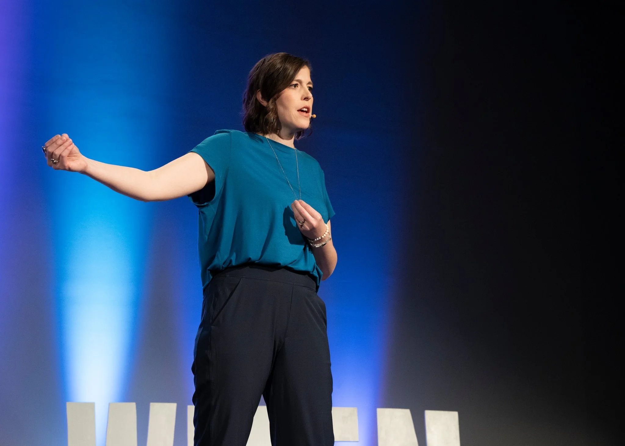 A woman speaking on stage against a blue and black background.