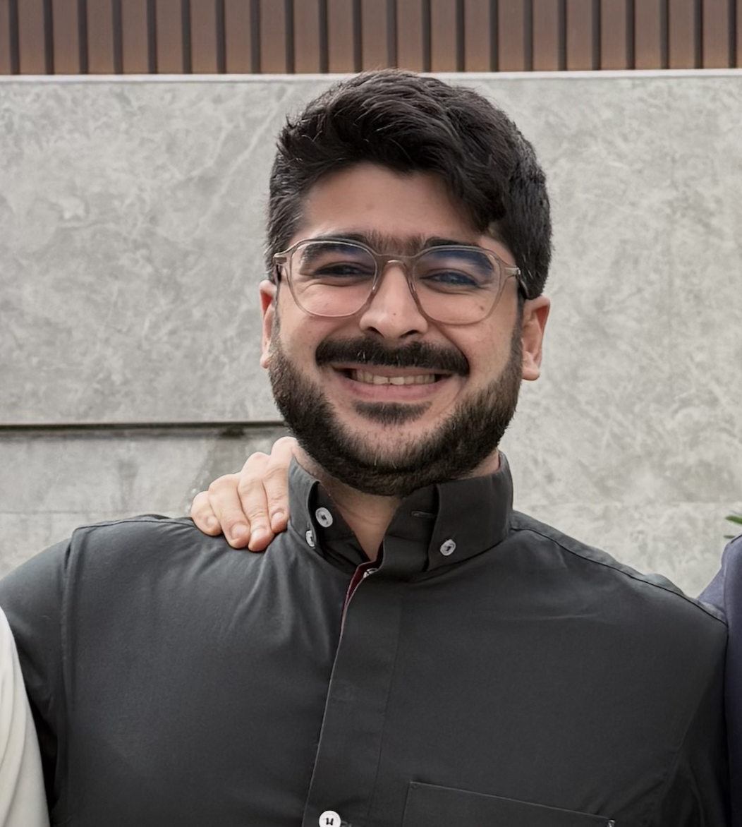 Smiling man with glasses and a beard, wearing a black shirt, standing outdoors.