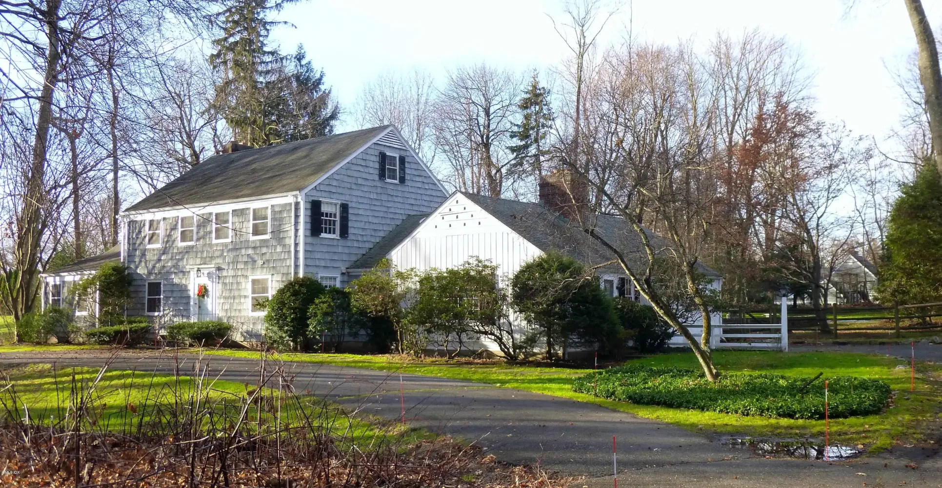 A white house with a gabled roof, shingle siding, and black shutters, surrounded by leafless trees and a green lawn.