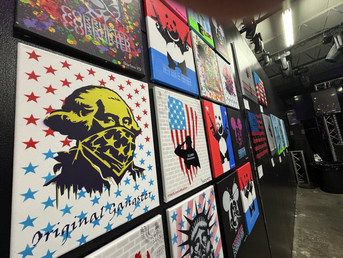 A display wall with various colorful protest and pop art posters, including images of a masked person with American flag elements, and other pop culture and political messages.