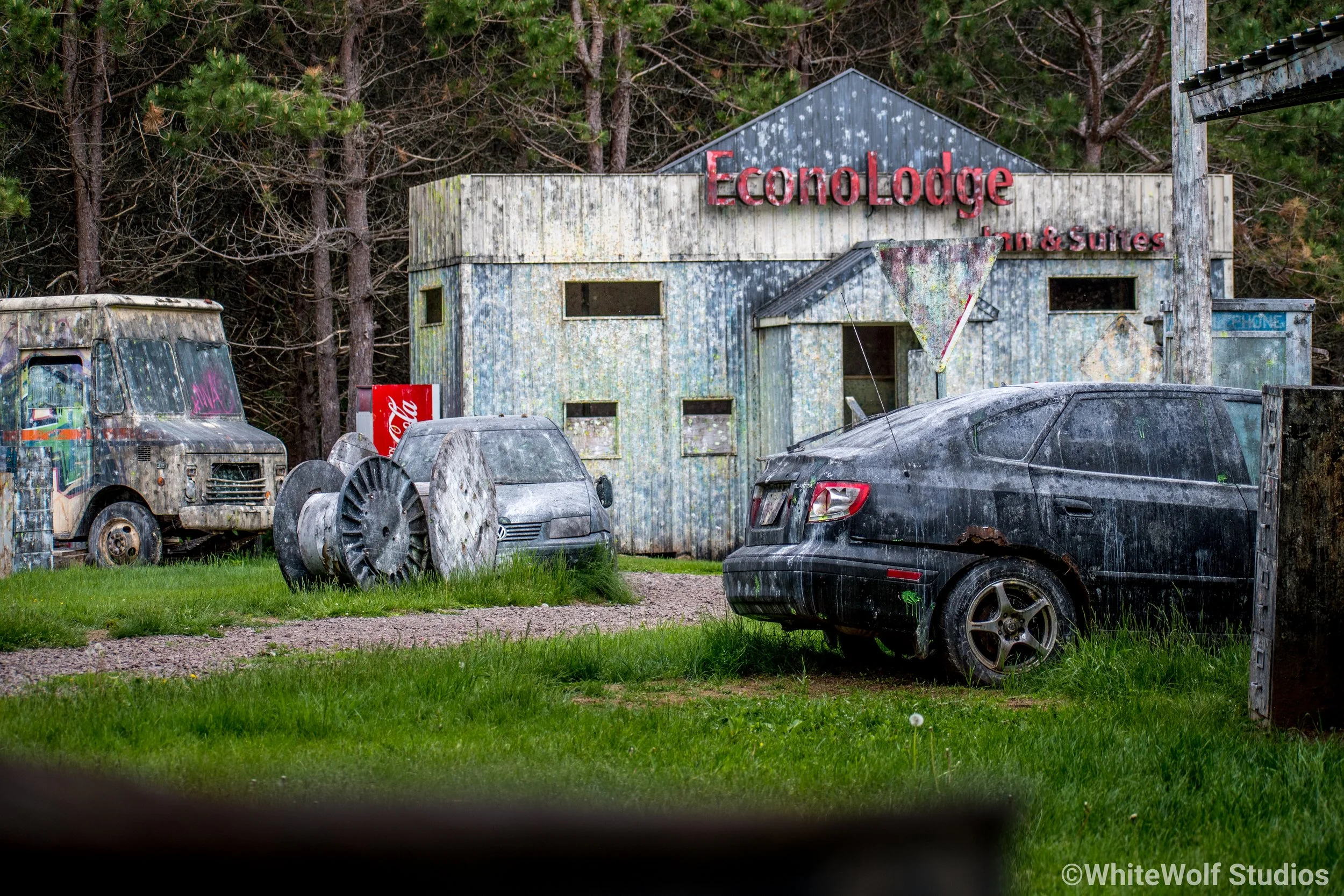 Old, abandoned vehicles and a dilapidated building with a sign for EconoLodge in a wooded area.