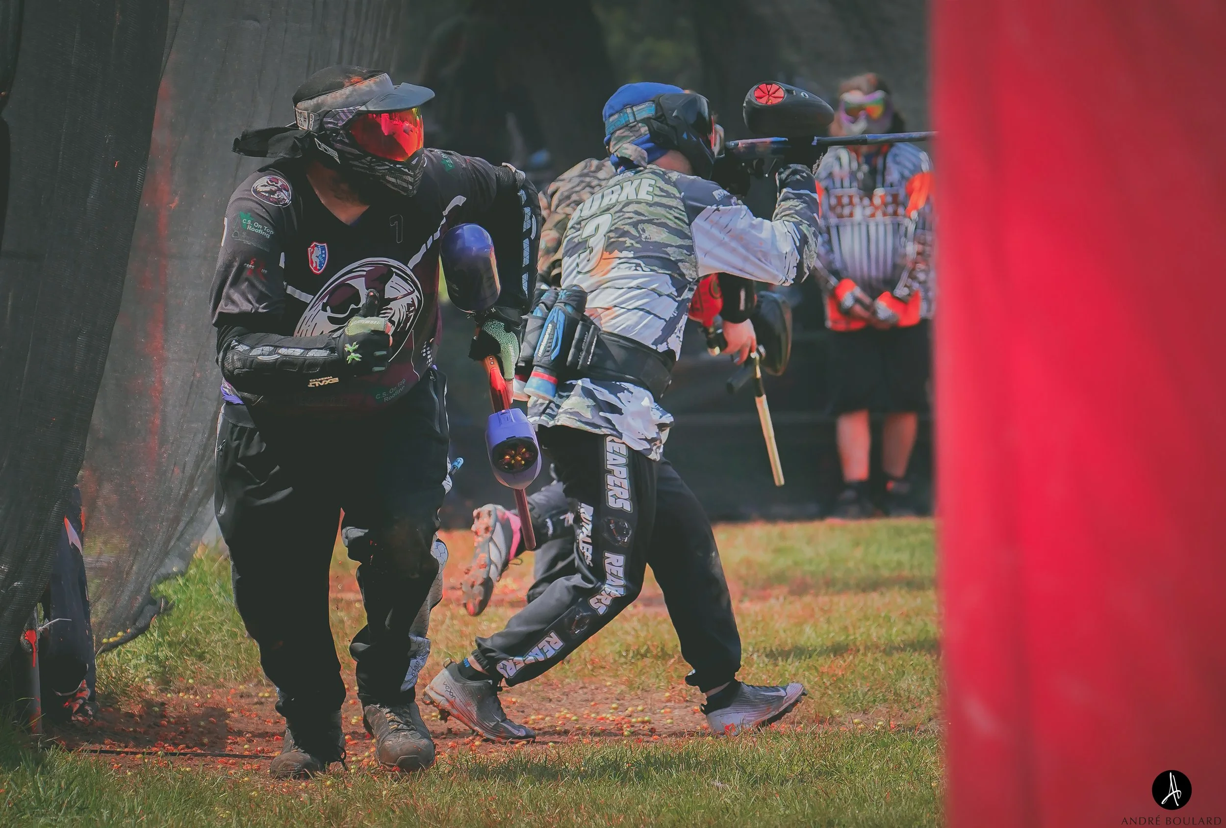 Series of paintball players in camouflage and athletic gear taking cover behind a barrier during a paintball game outdoors.