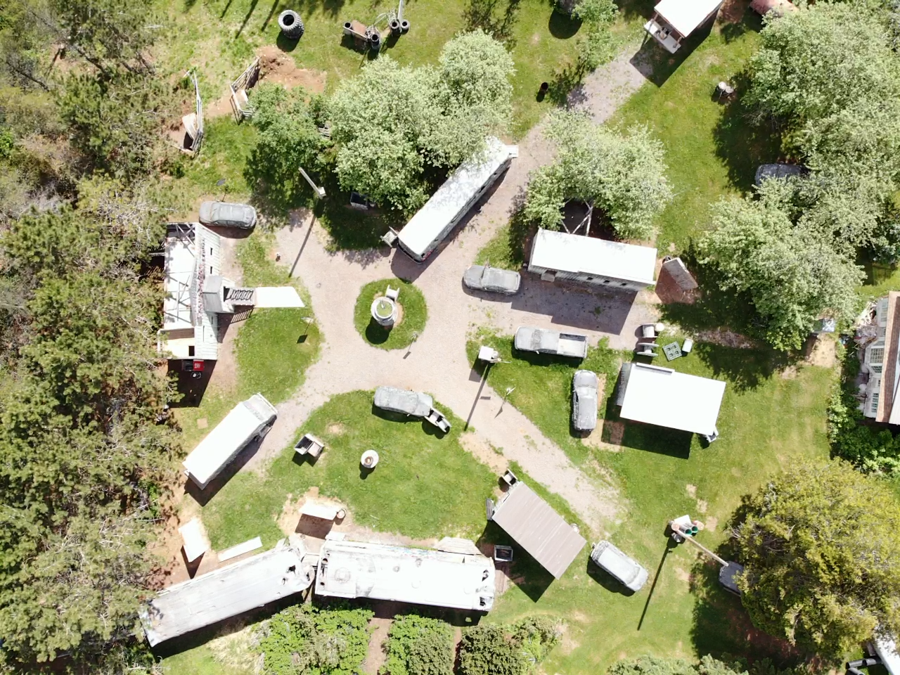 An aerial view of a yard with trees, several trailers, vehicles, and small structures, including a fire hydrant and picnic tables.