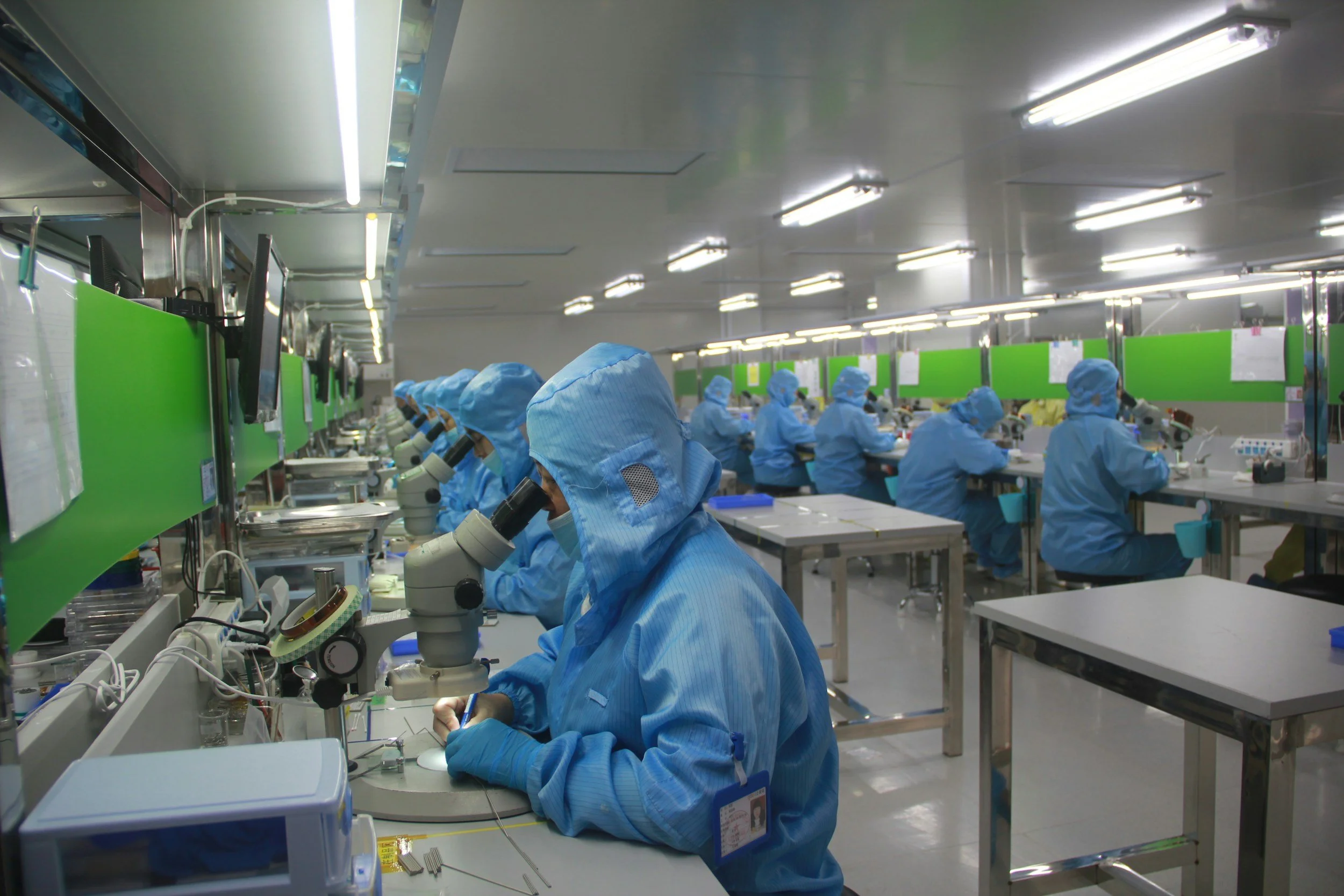 Scientists in blue protective suits working at microscopes in a laboratory.