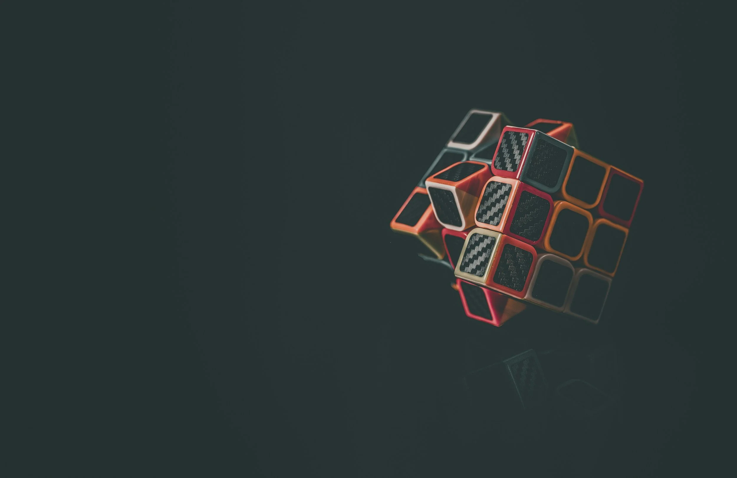 Colorful Rubik's cube with black, red, yellow, white, and orange sides on a dark reflective surface.